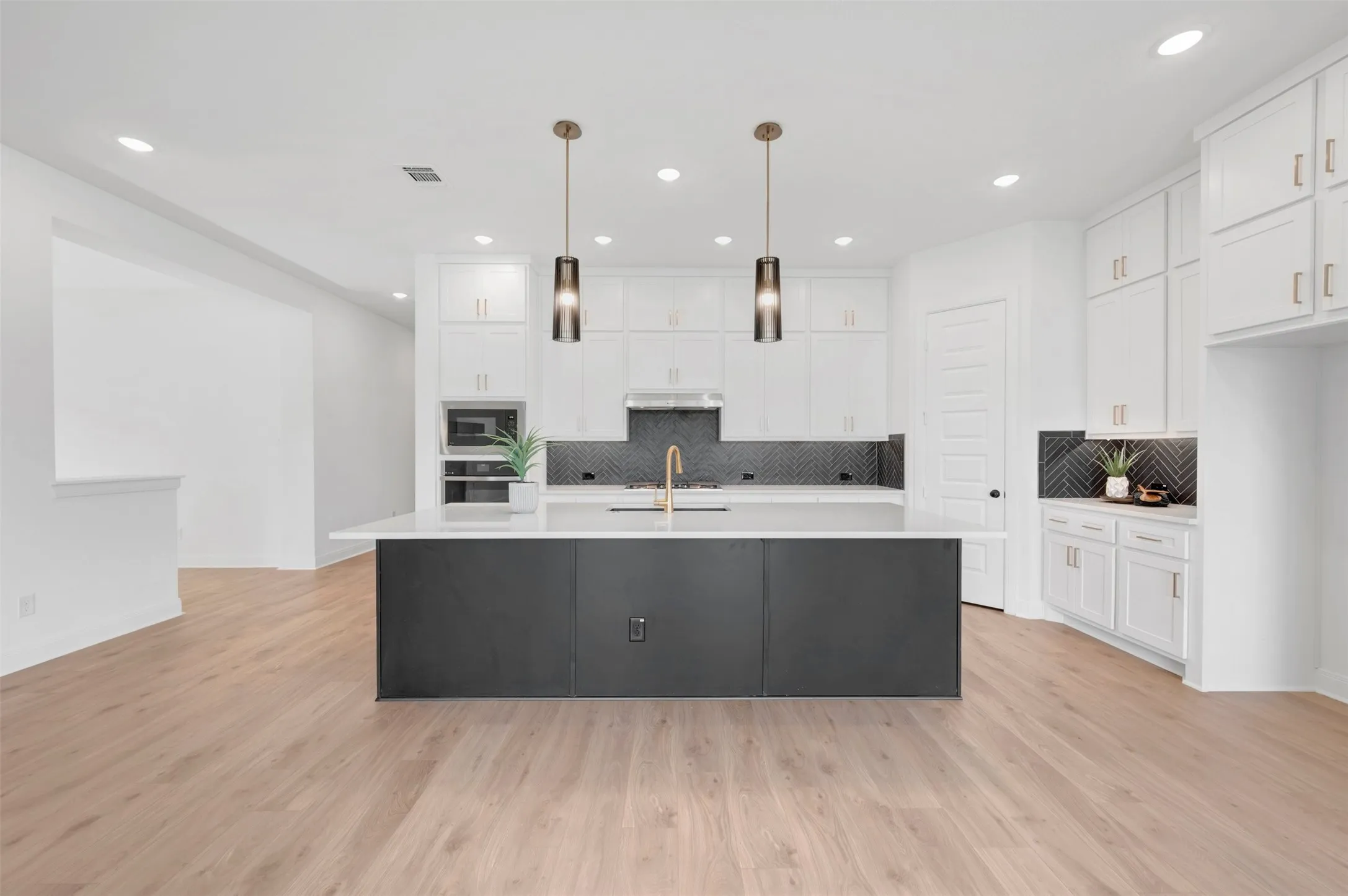 Kitchen featuring a dark-toned island with a white countertop, recessed lighting, wood-finish flooring, and white cabinetry with gold-toned​​‌​​​​‌​​‌‌​‌‌​​​‌‌​‌​‌​‌​​​‌​​ hardware