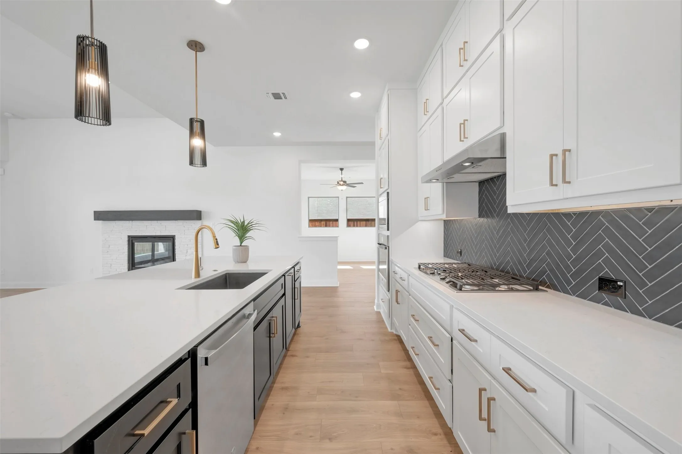 Kitchen featuring a gas range, herringbone tile backsplash, white cabinetry, and a large island with an undermount sink and gold-finish faucet