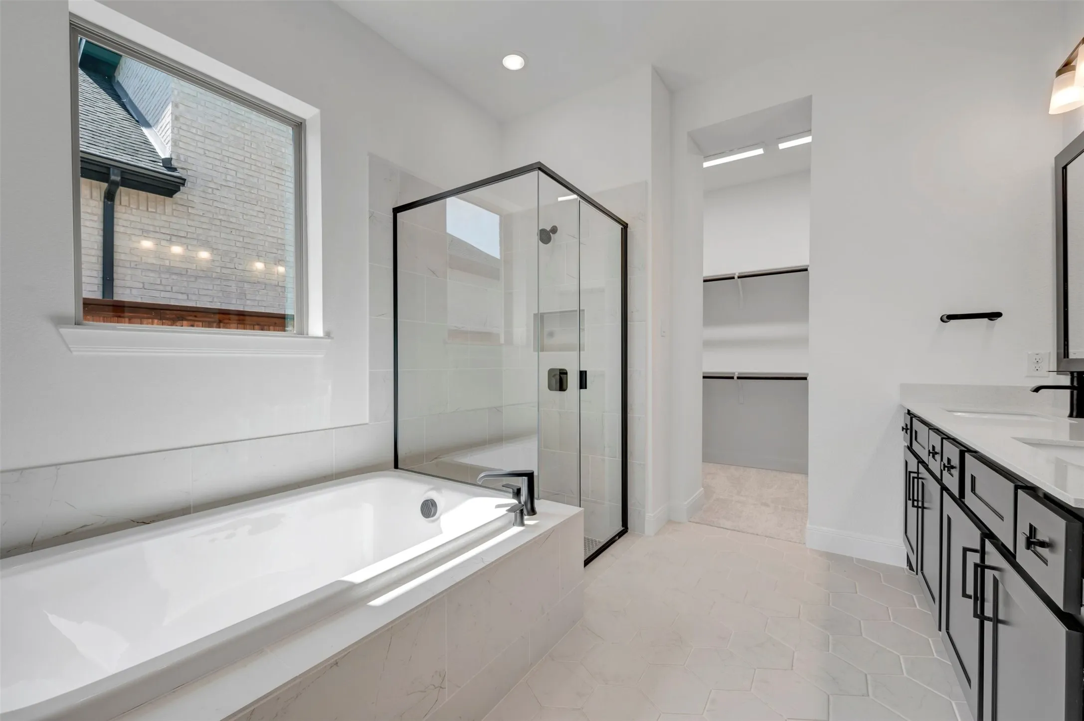 Frameless glass shower enclosure, built-in bathtub, dual vanity with undermount sinks, hexagon tile flooring, and recessed lighting