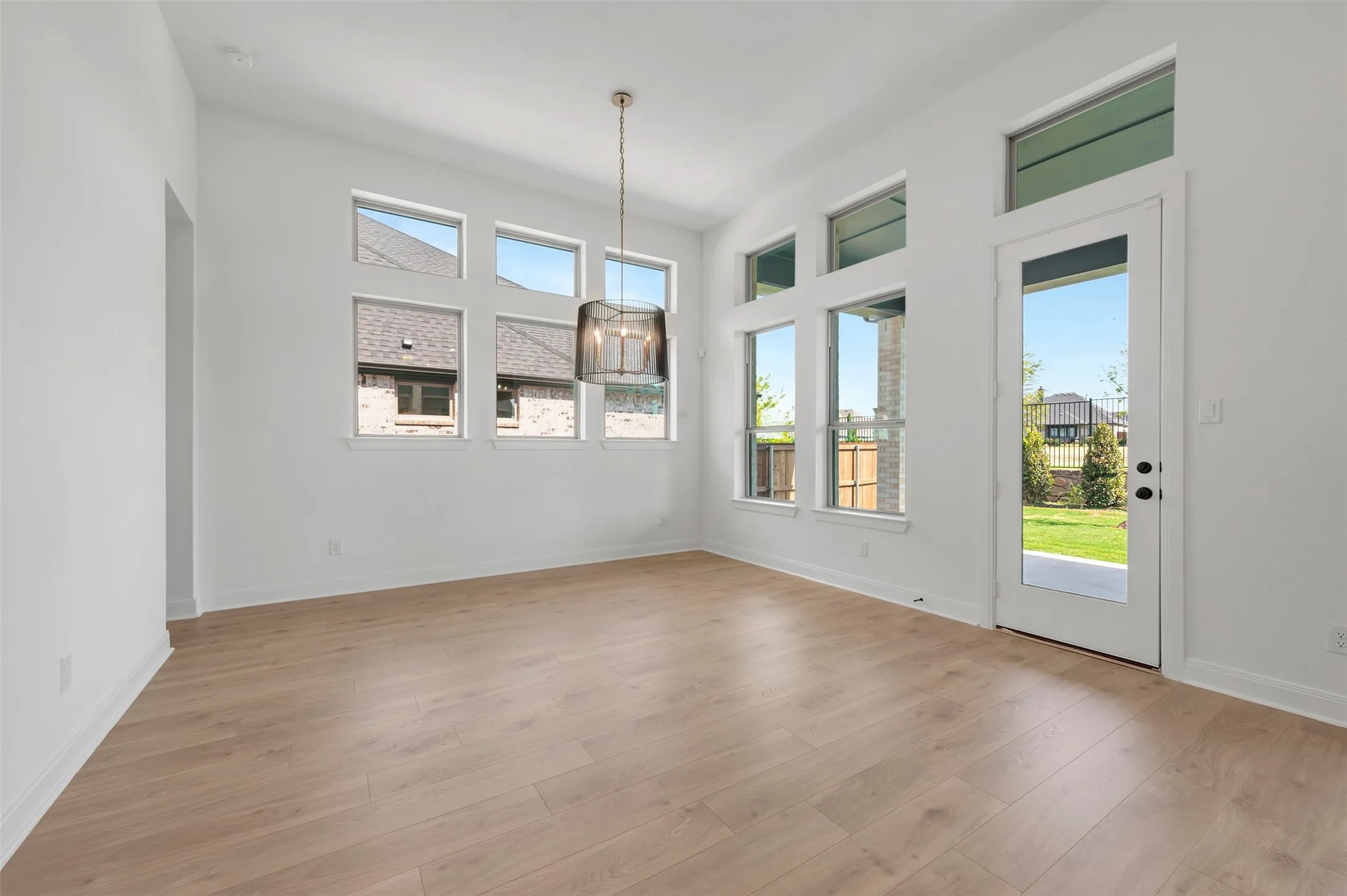 Spacious interior featuring high ceilings, wood-finish flooring, a contemporary pendant light fixture, and abundant natural illumination from multiple windows and a glass-paneled door