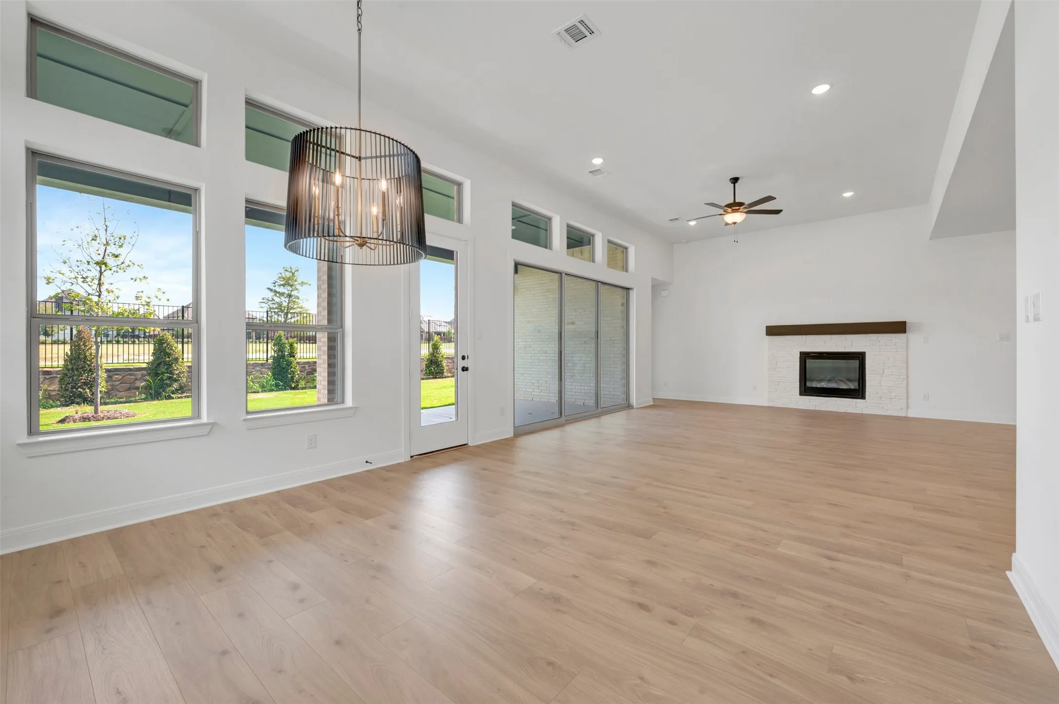 Vaulted ceilings with recessed lighting, wood-finish flooring, a modern linear fireplace with a textured surround, and a contemporary chandelier