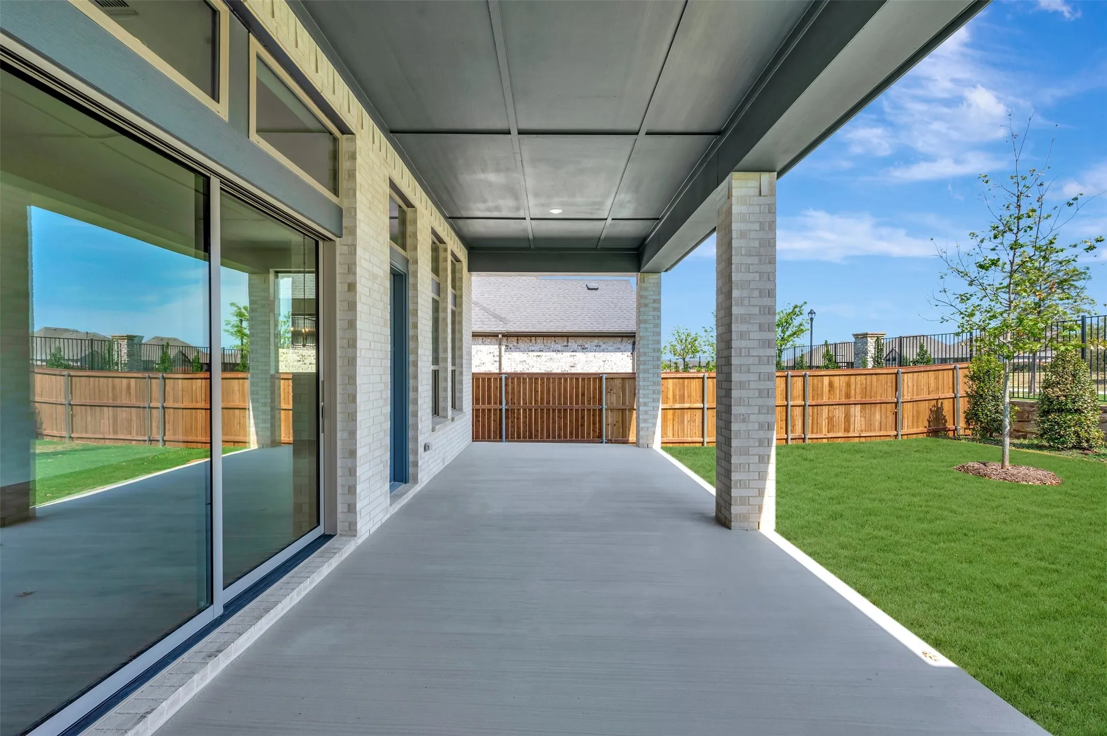 Covered patio with a painted concrete surface, brick columns, and a white brick exterior