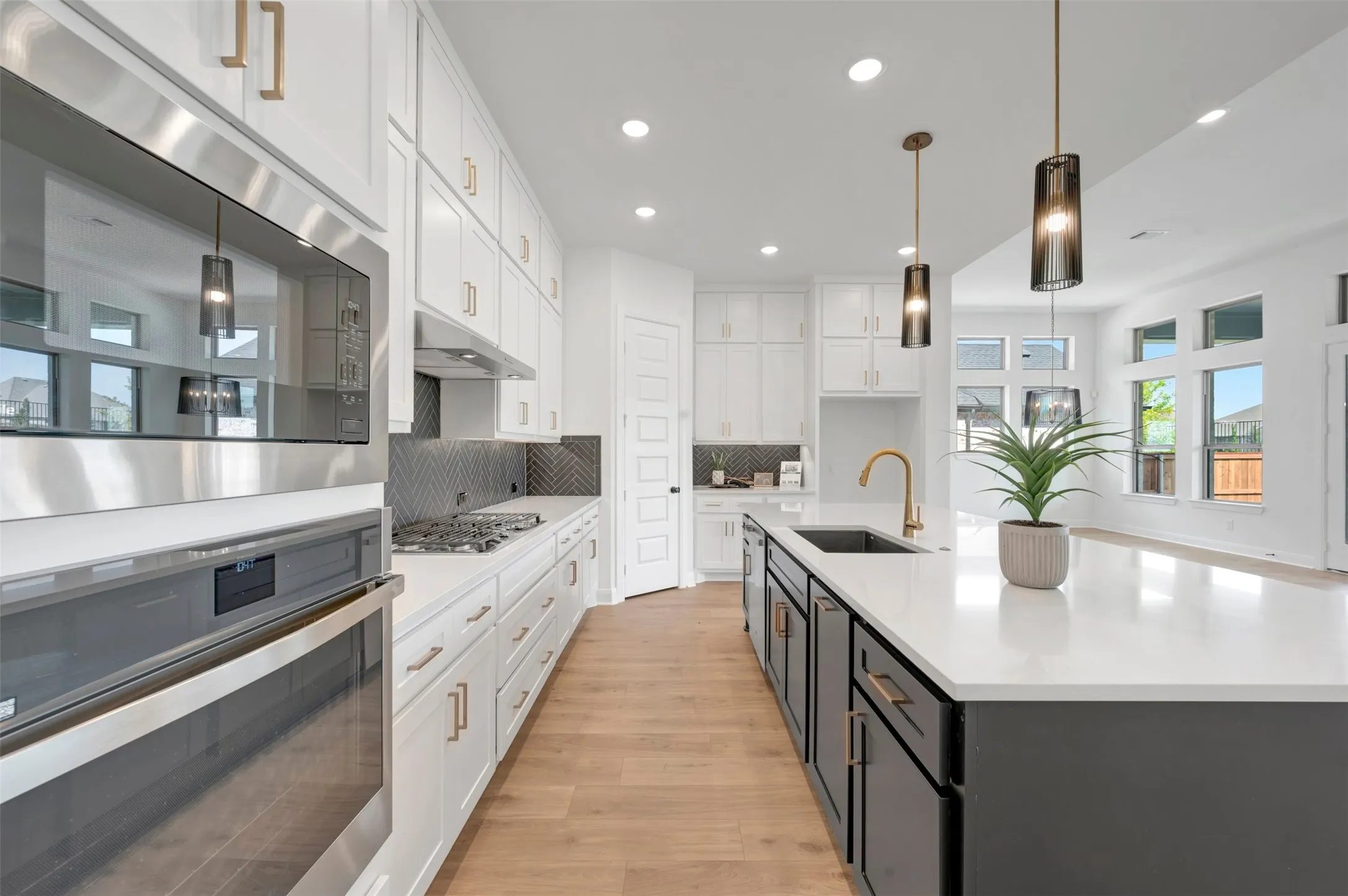 Spacious kitchen featuring an expansive island with a built-in sink, stainless steel appliances, white cabinetry with gold-tone hardware, and wood-finish flooring