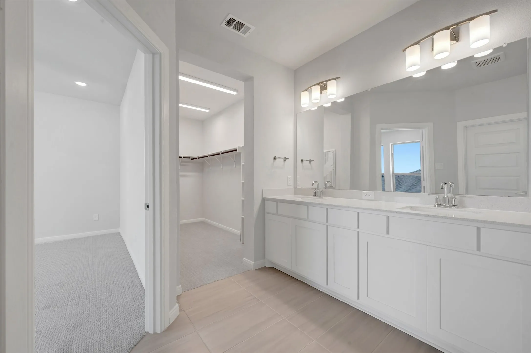 Bathroom featuring a double vanity with white cabinetry, light-toned countertops, and a full-width mirror with dual sconce lighting