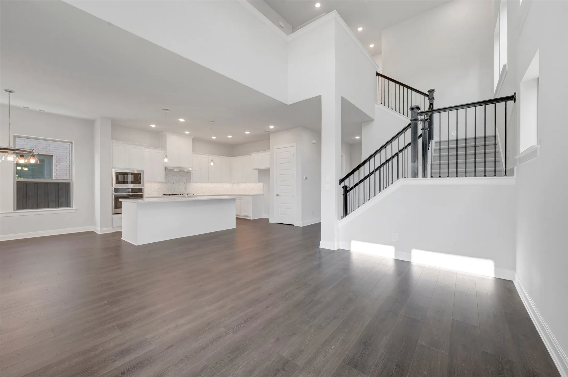 Spacious open-concept interior featuring wood-finish flooring, a two-story ceiling, and a modern kitchen with a large island