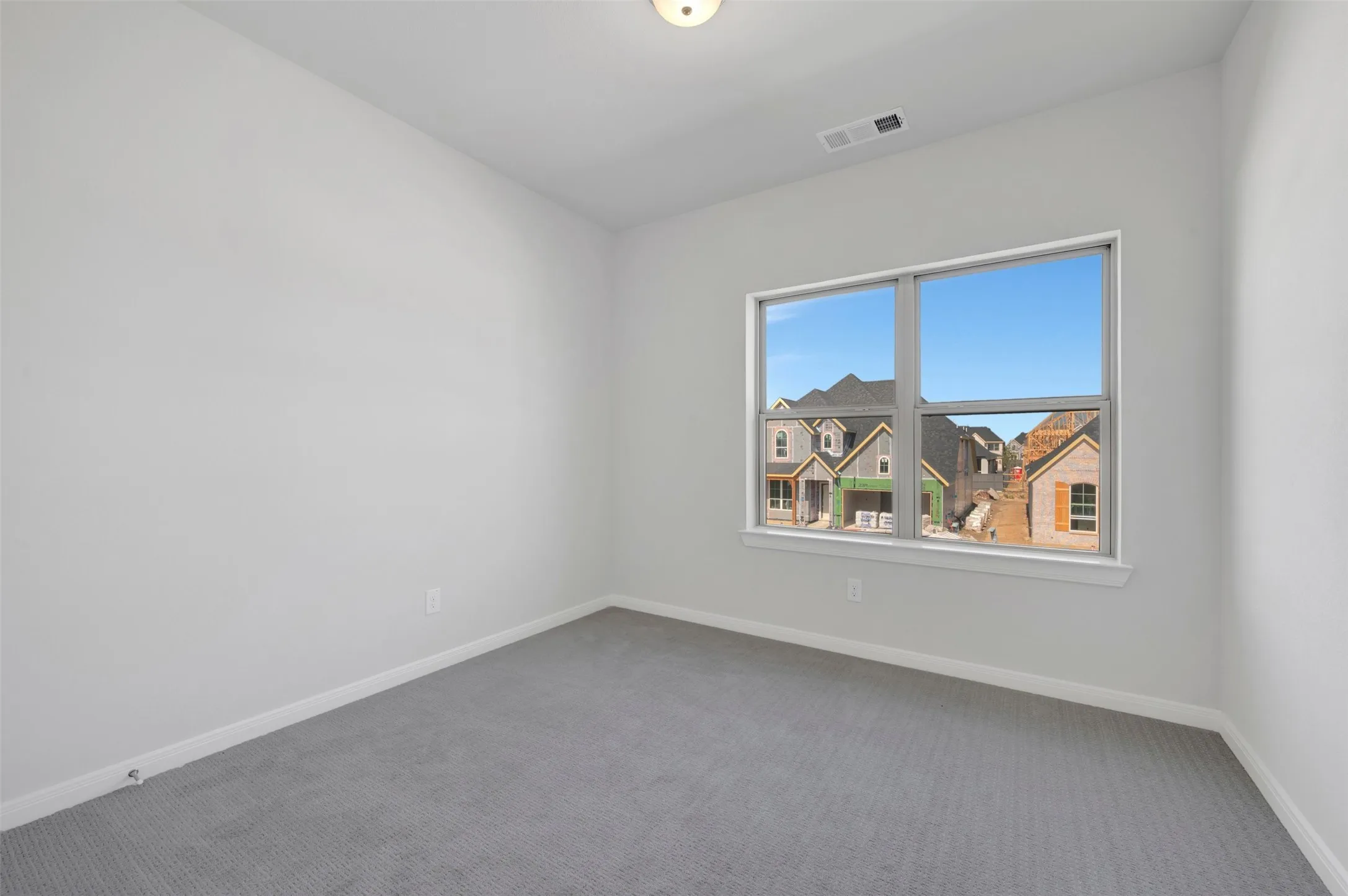 Spacious room featuring light gray carpeting, neutral wall paint, and a large window with white trim