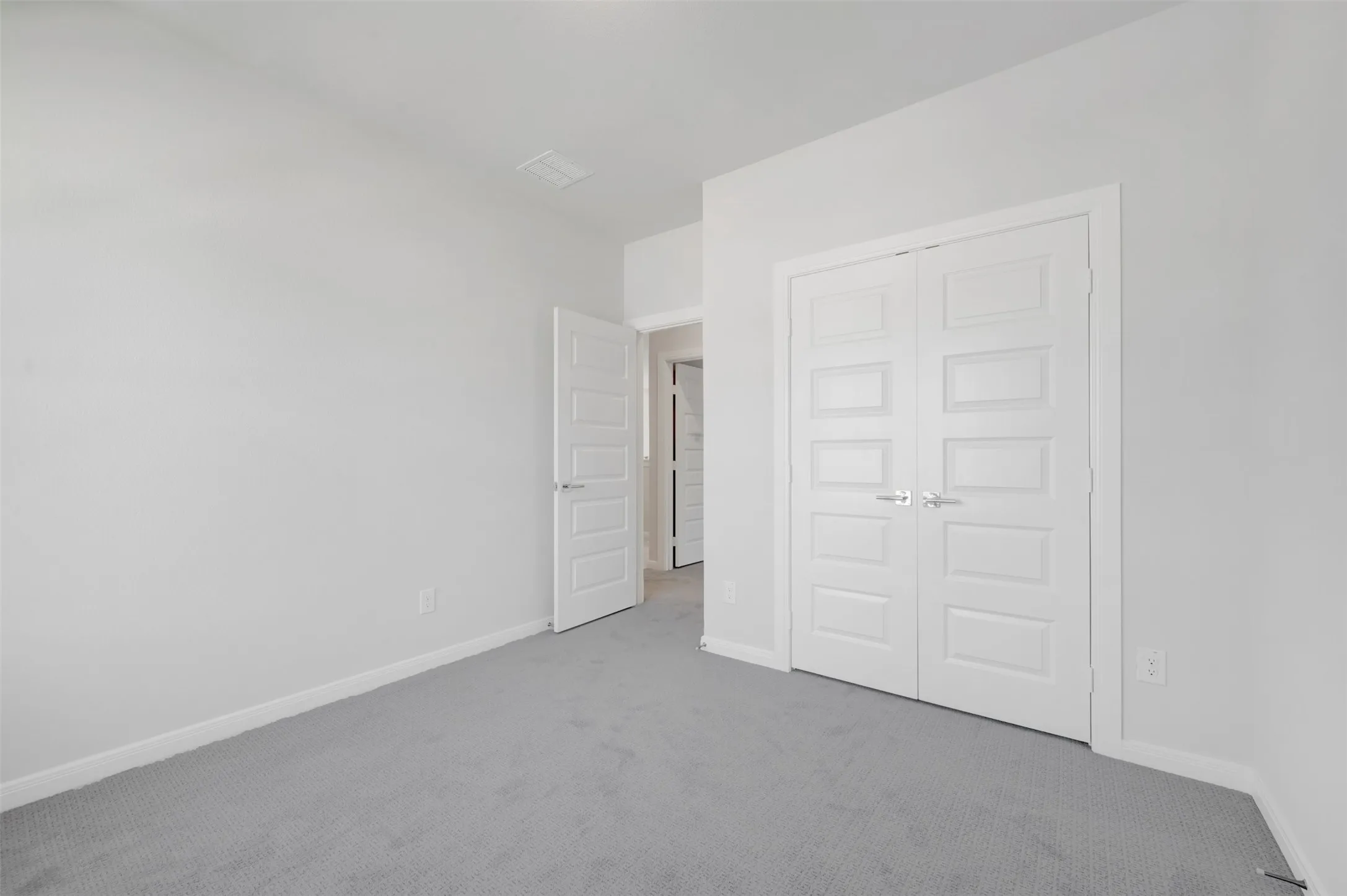 Bedroom featuring light gray carpeting, white baseboards, and a white interior door with panel detailing