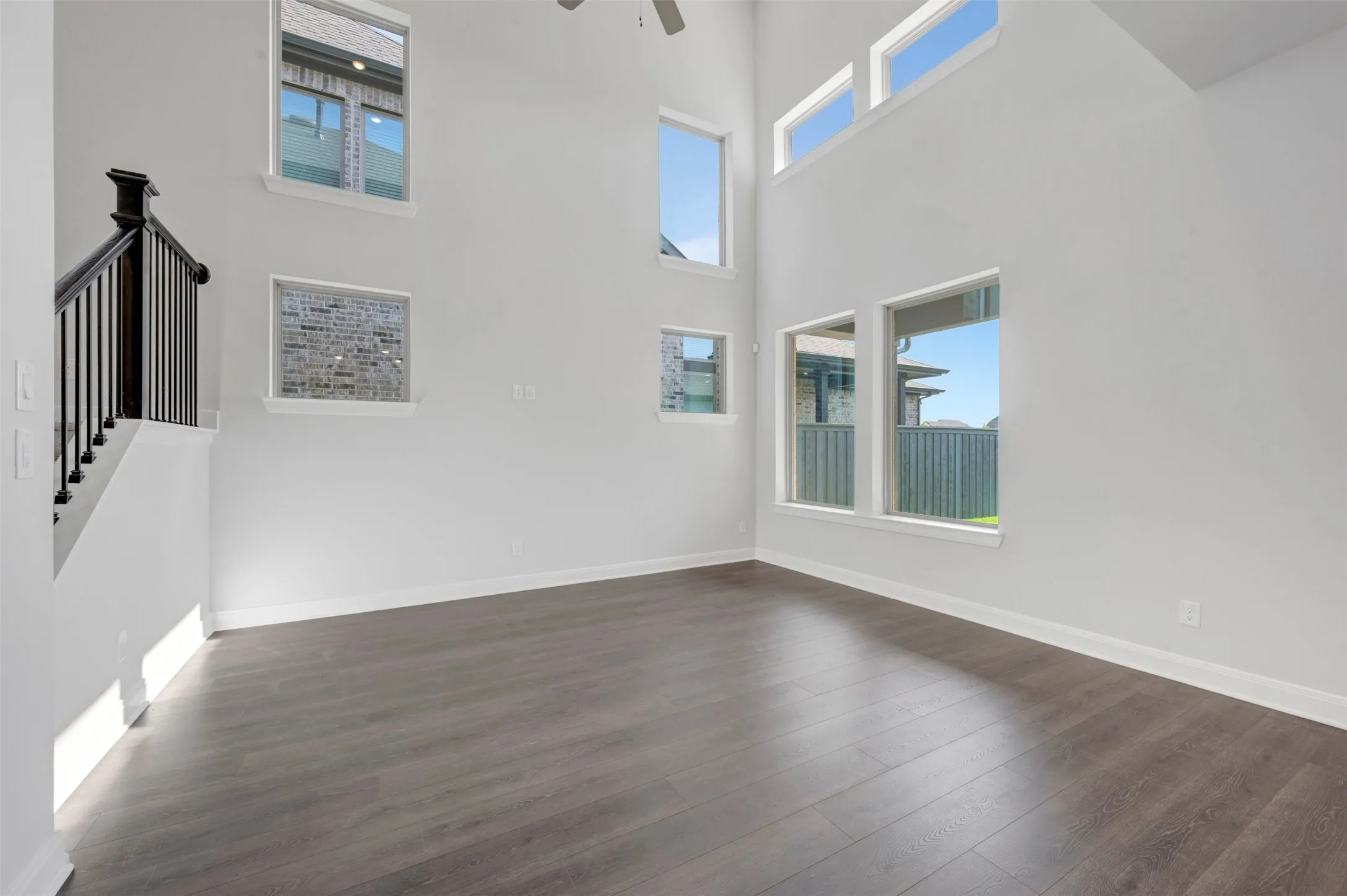 Spacious interior featuring a two-story ceiling, dark wood-finish flooring, multiple large windows, clean white walls, and a staircase with dark wood newel post and balusters