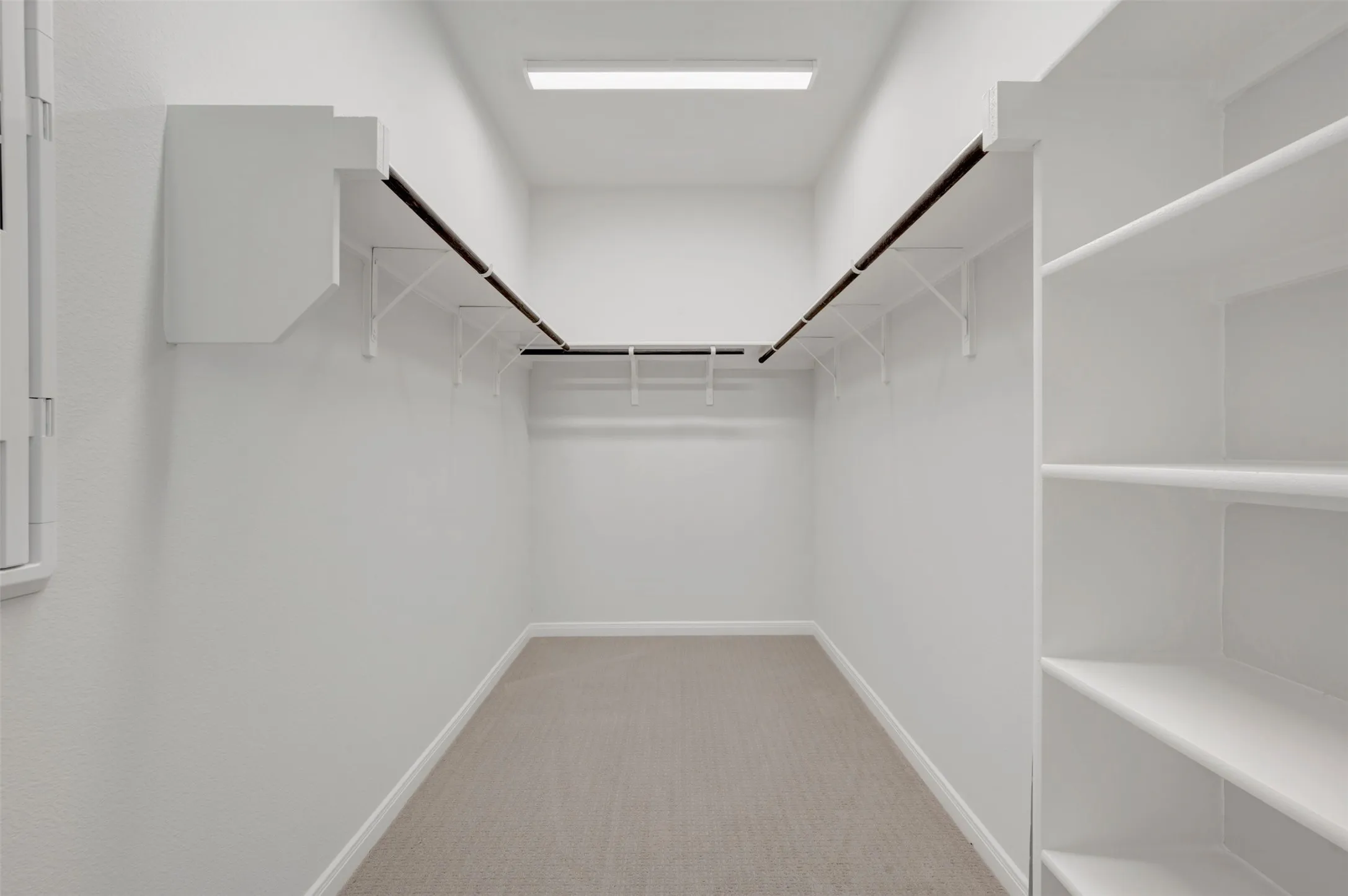 Spacious walk-in closet featuring built-in shelving, multiple hanging rods, wall-mounted storage, light-toned carpeting, and recessed lighting
