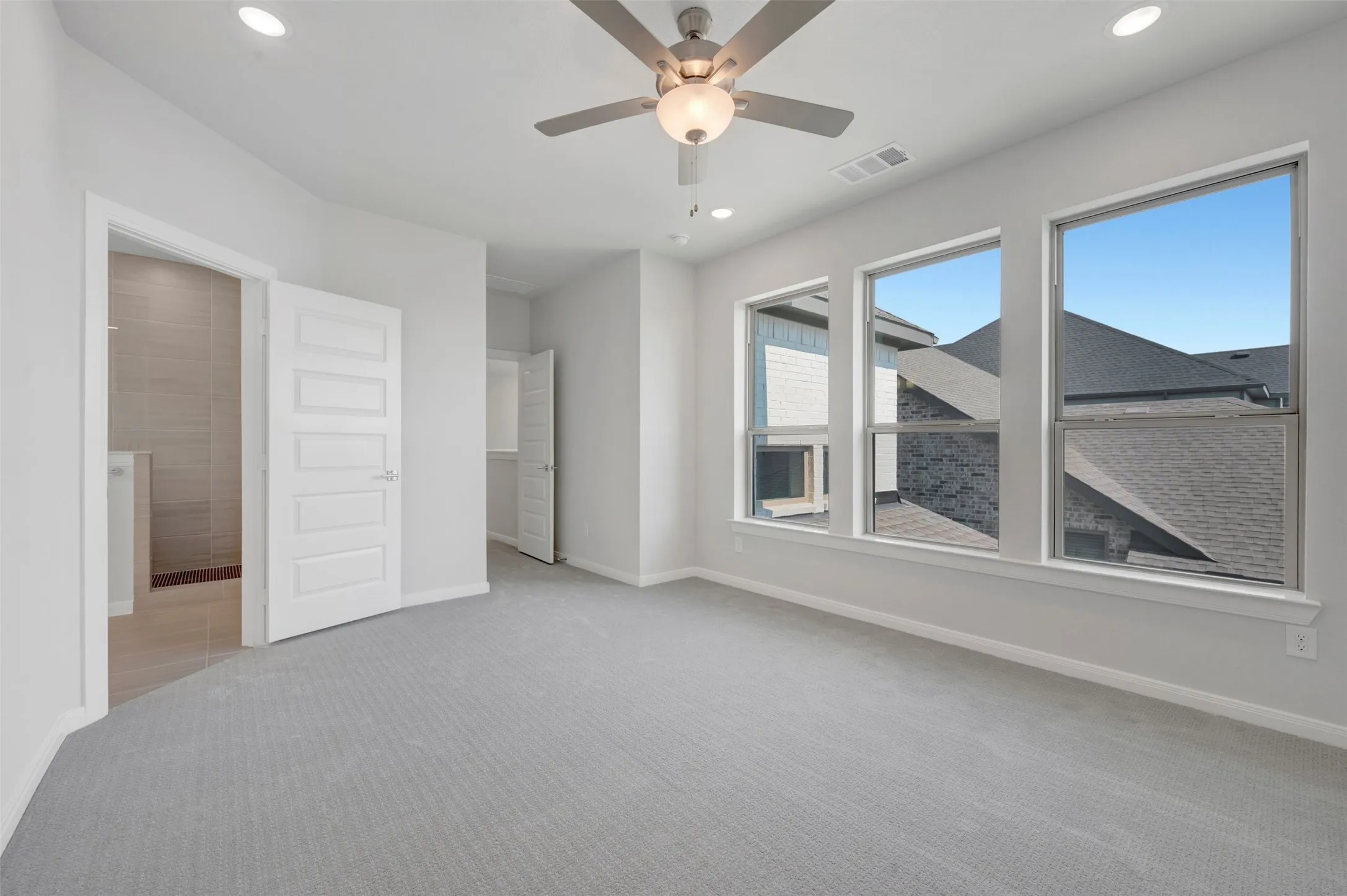 Spacious room featuring light gray carpeting, three large windows, a ceiling fan with integrated lighting, and recessed ceiling lights