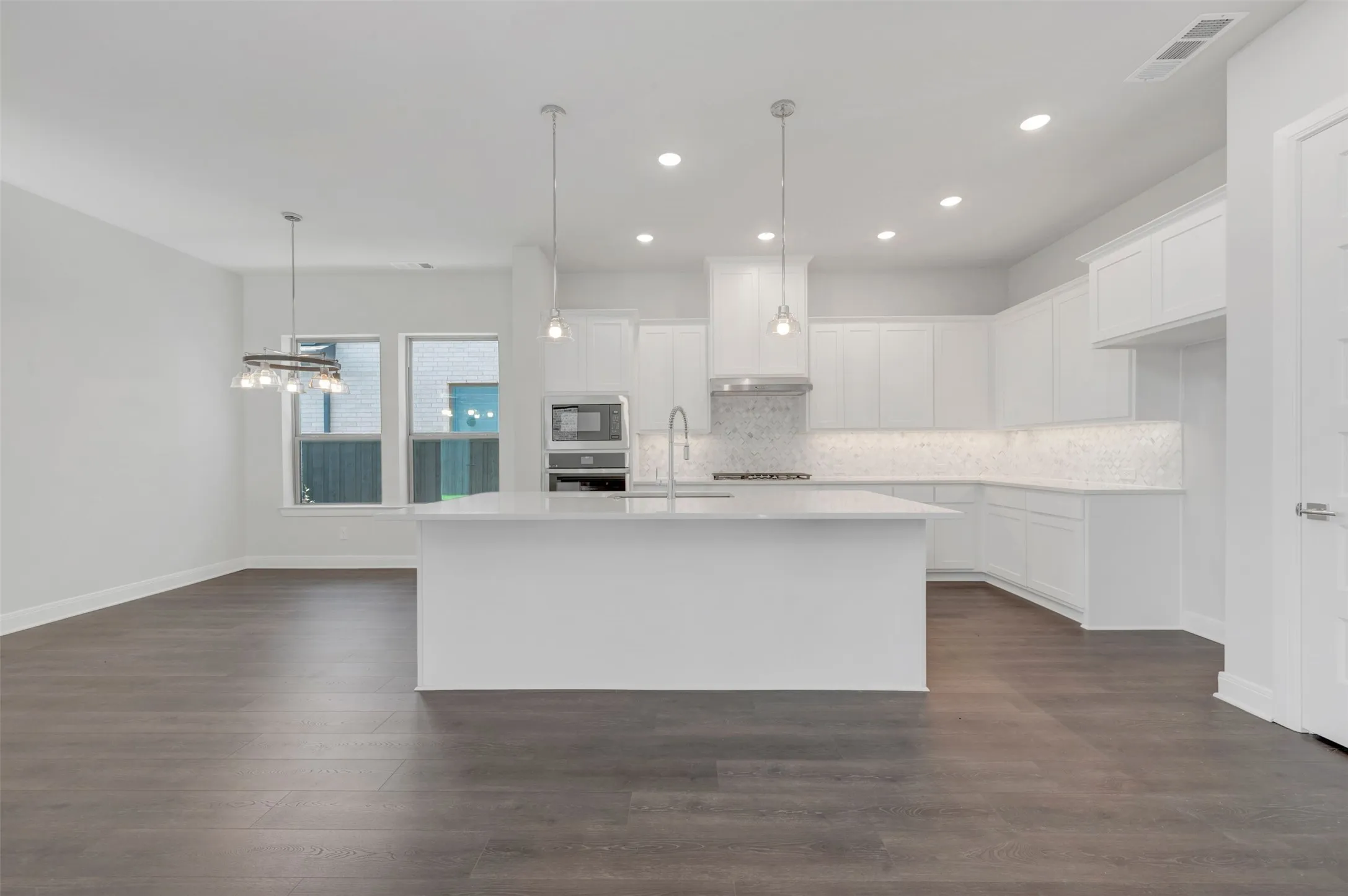Open-concept living area featuring dark wood-finish flooring, a contemporary chandelier, recessed lighting, and an expansive white kitchen island