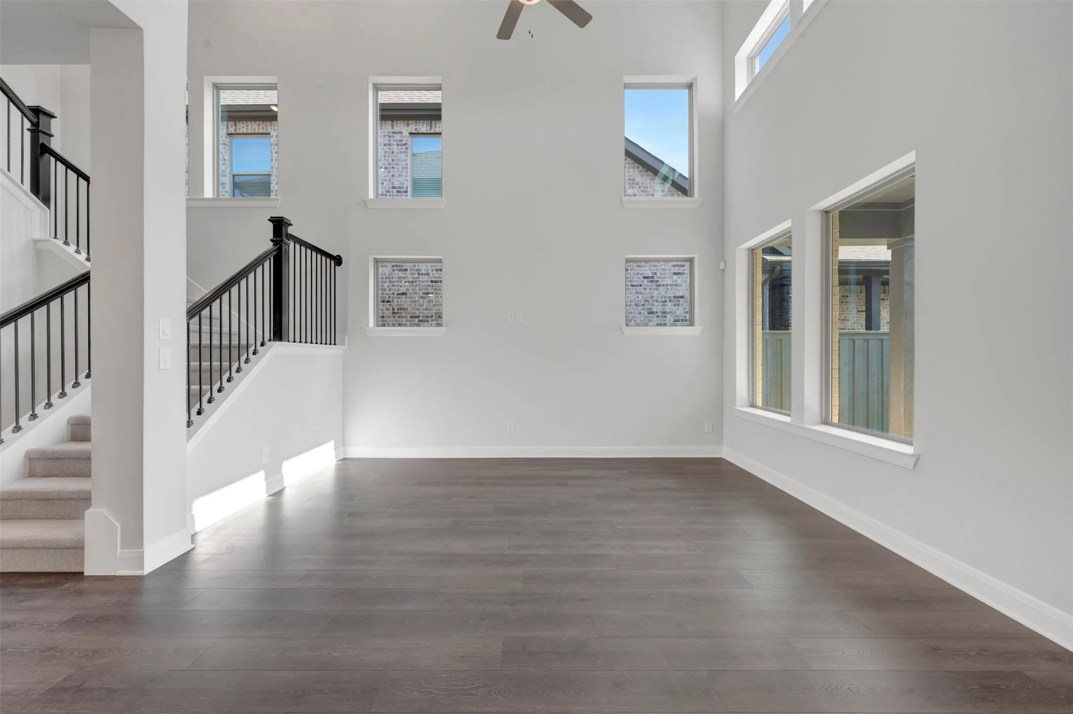 Spacious living area featuring high ceilings, dark wood-finish flooring, and multiple windows