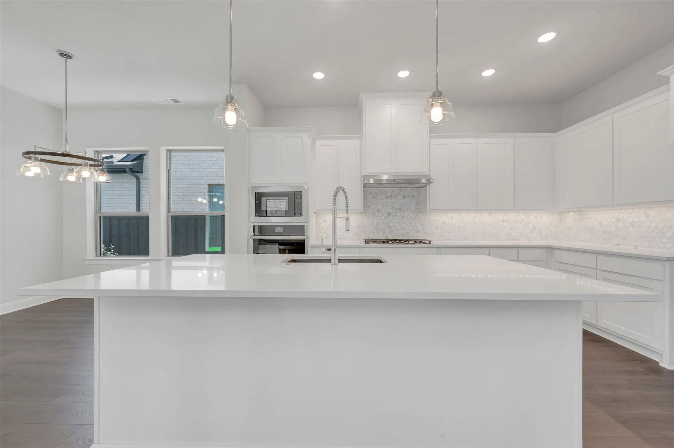 Modern kitchen featuring an expansive island with a built-in sink, white cabinetry, integrated stainless steel appliances, a tiled backsplash, and recessed lighting