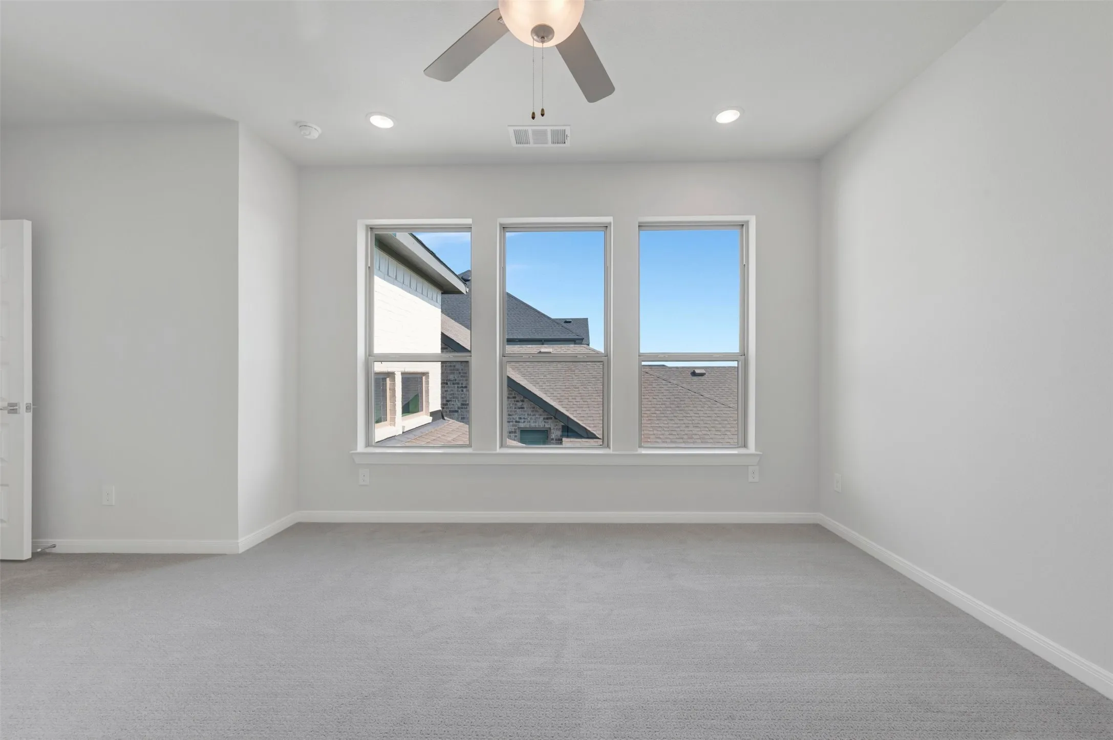 Spacious room featuring three large windows, gray carpeting, neutral wall paint, and white trim
