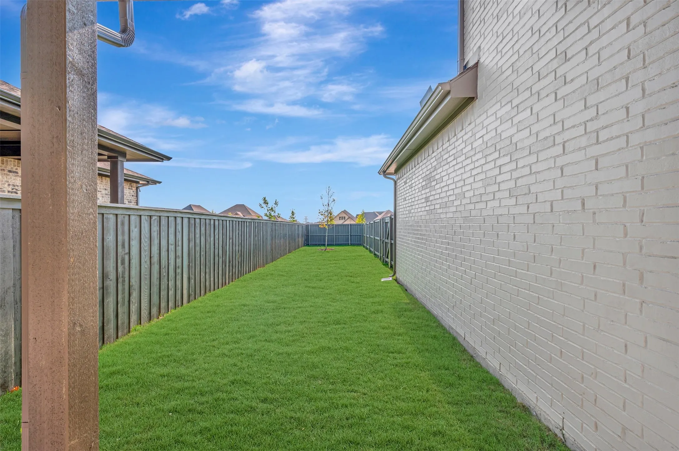Green lawn area bordered by a wood privacy fence and a painted brick exterior wall
