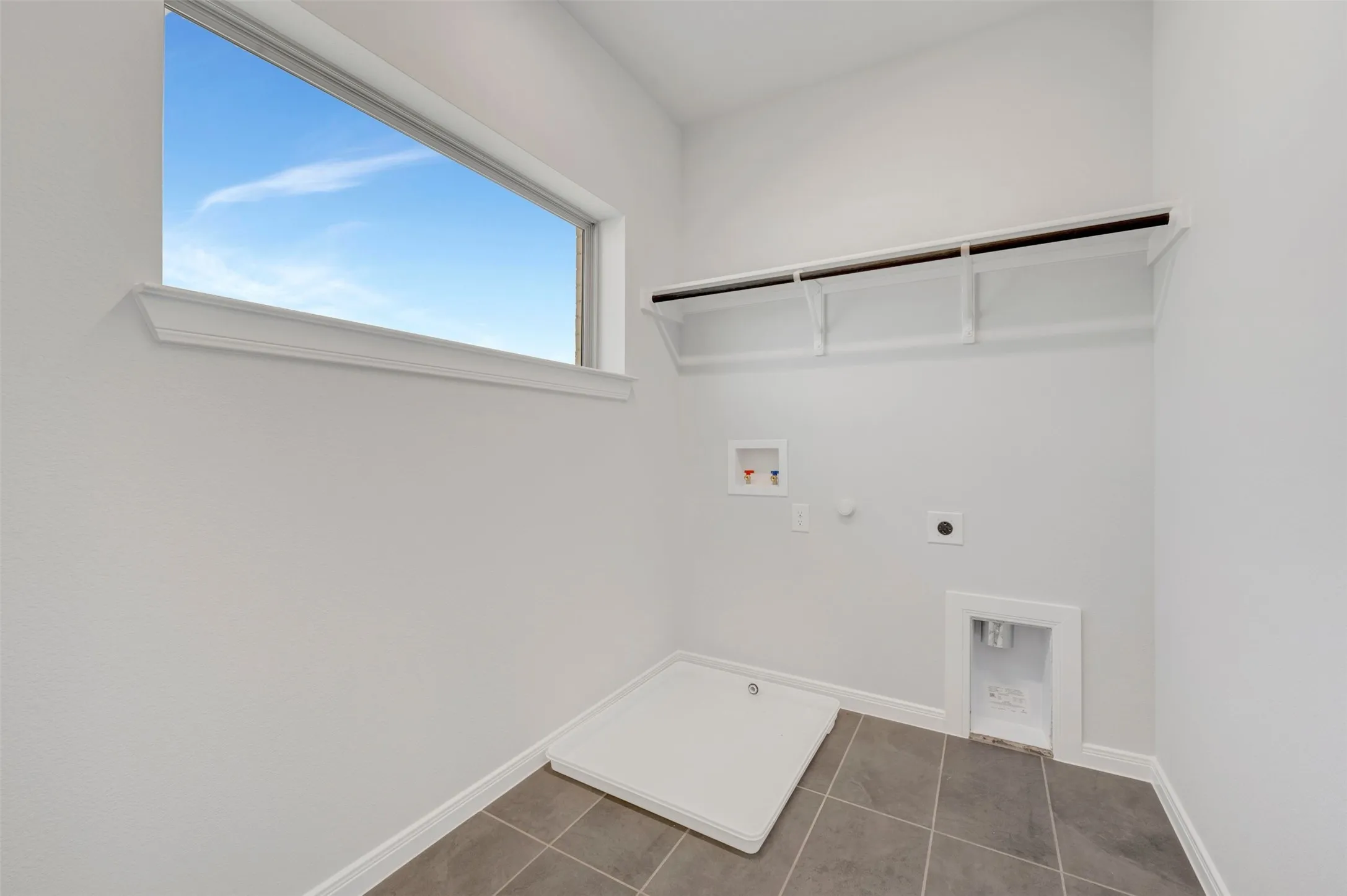 Utility room featuring a horizontal window, built-in shelving, white walls, and gray tile flooring
