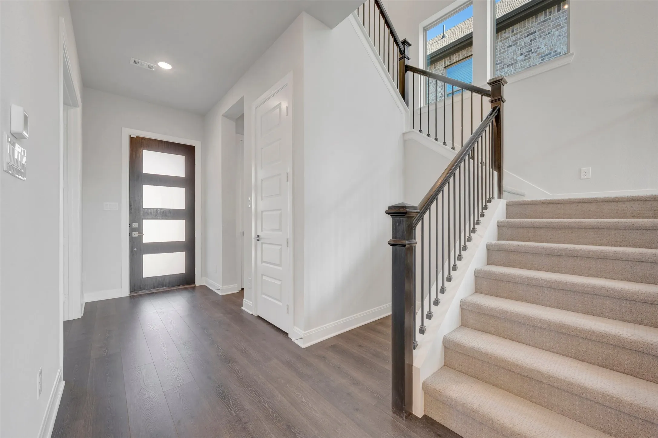 Entry foyer featuring wood-finish flooring, a modern front door with frosted glass panels, and a staircase with carpeted treads and wrought iron balusters