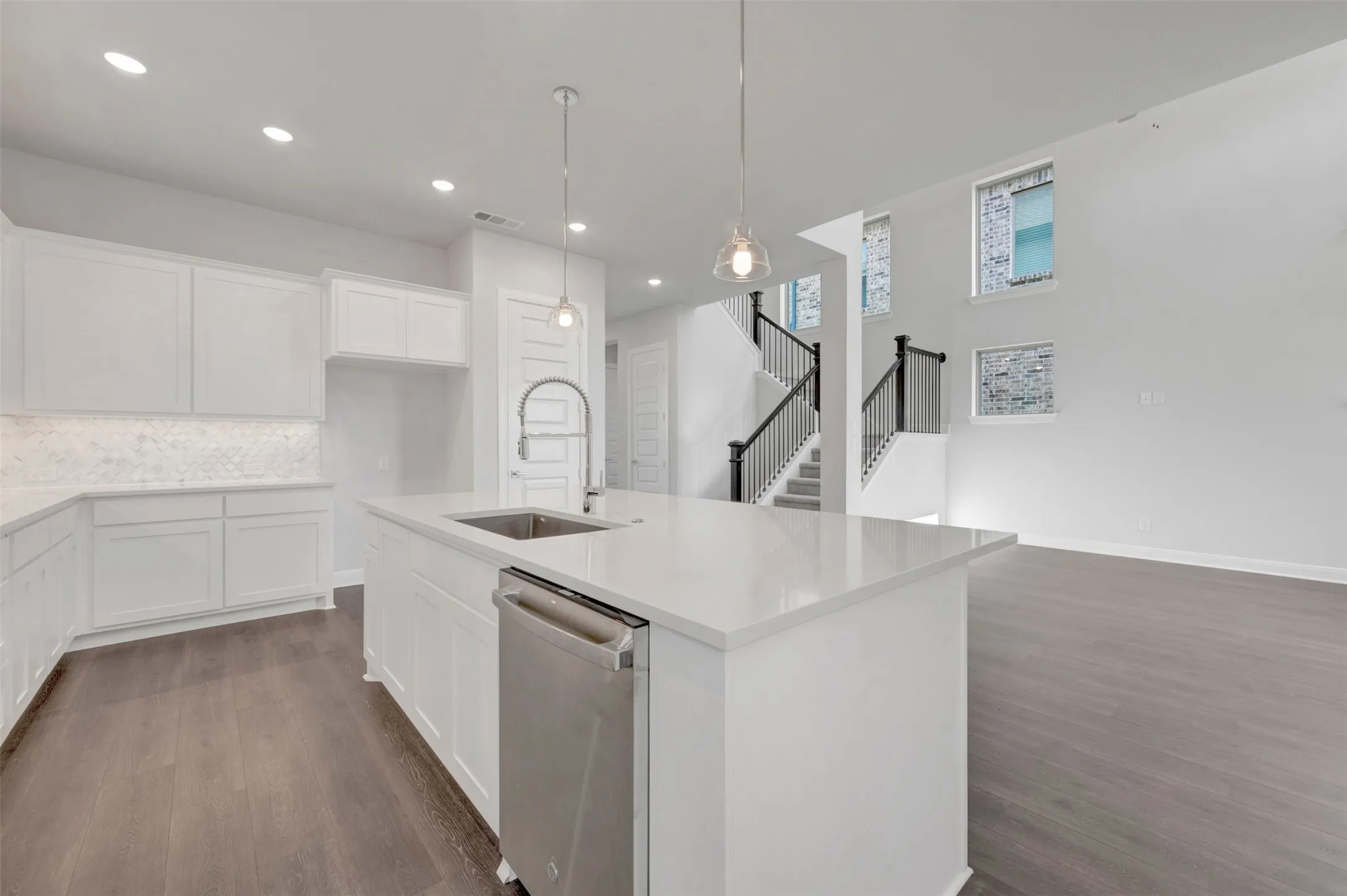 Open-concept kitchen featuring an island with a stainless steel sink, white cabinetry, and recessed lighting