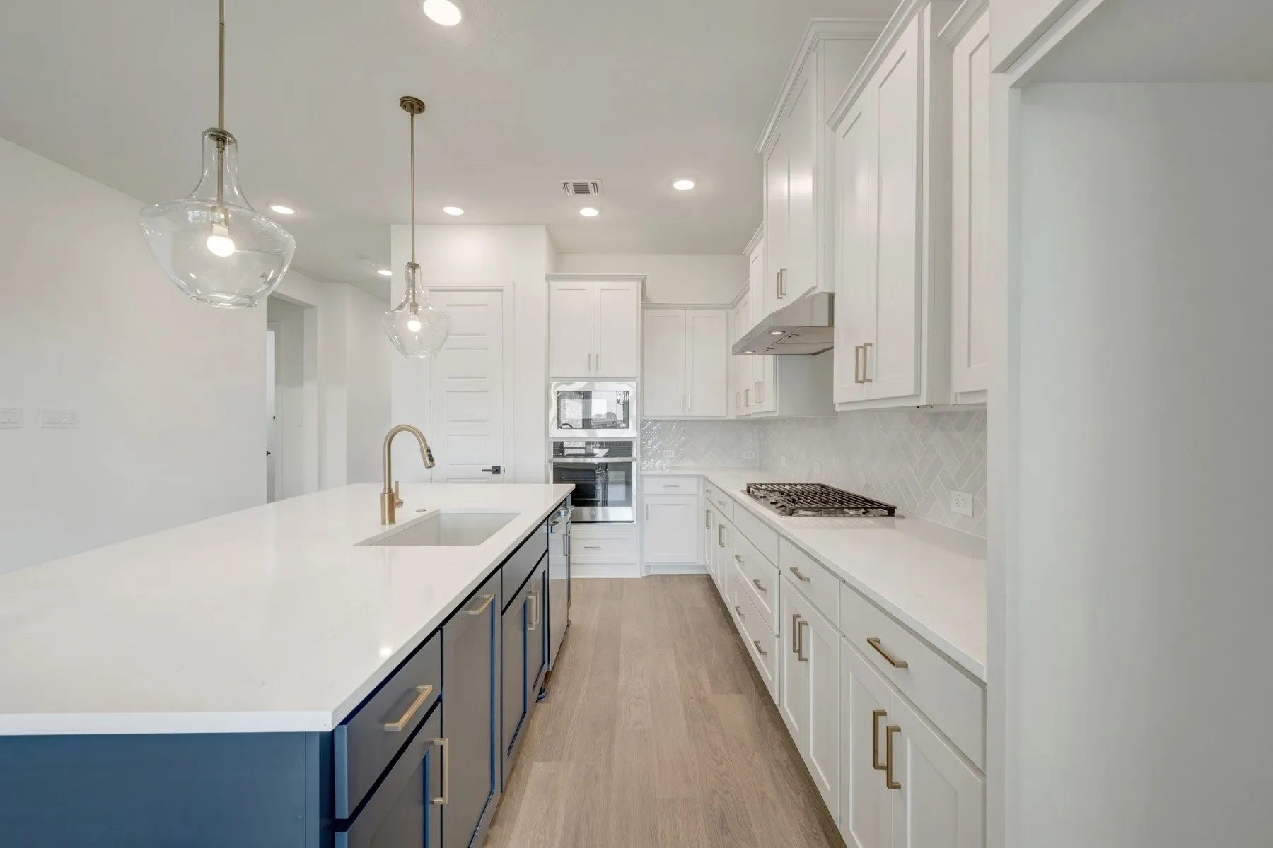 Kitchen featuring an expansive island with a built-in sink, white shaker cabinetry, stainless steel appliances, a gas cooktop, and wood-finish flooring