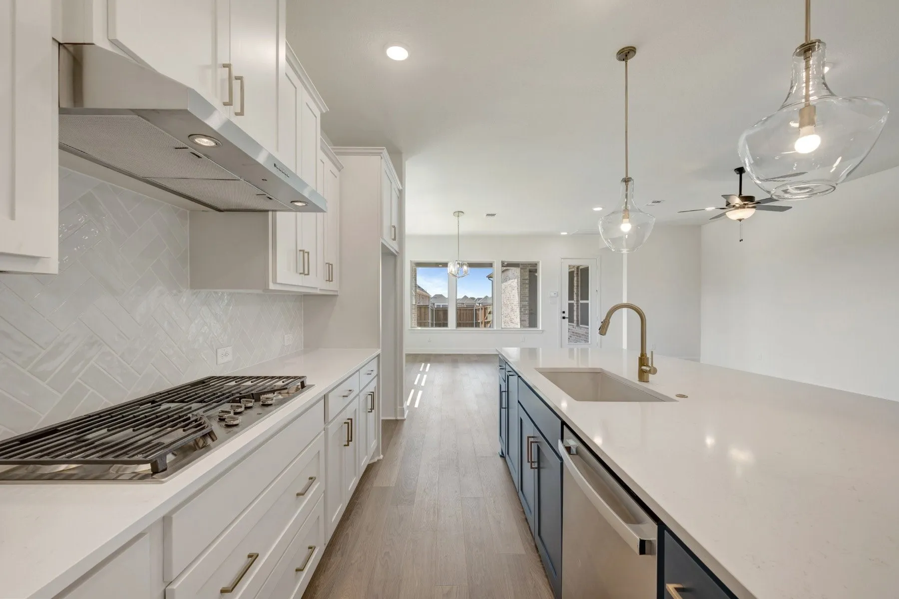 Kitchen featuring white shaker cabinetry, stainless steel range hood, herringbone tile backsplash, and an island with an integrated sink and pendant lighting