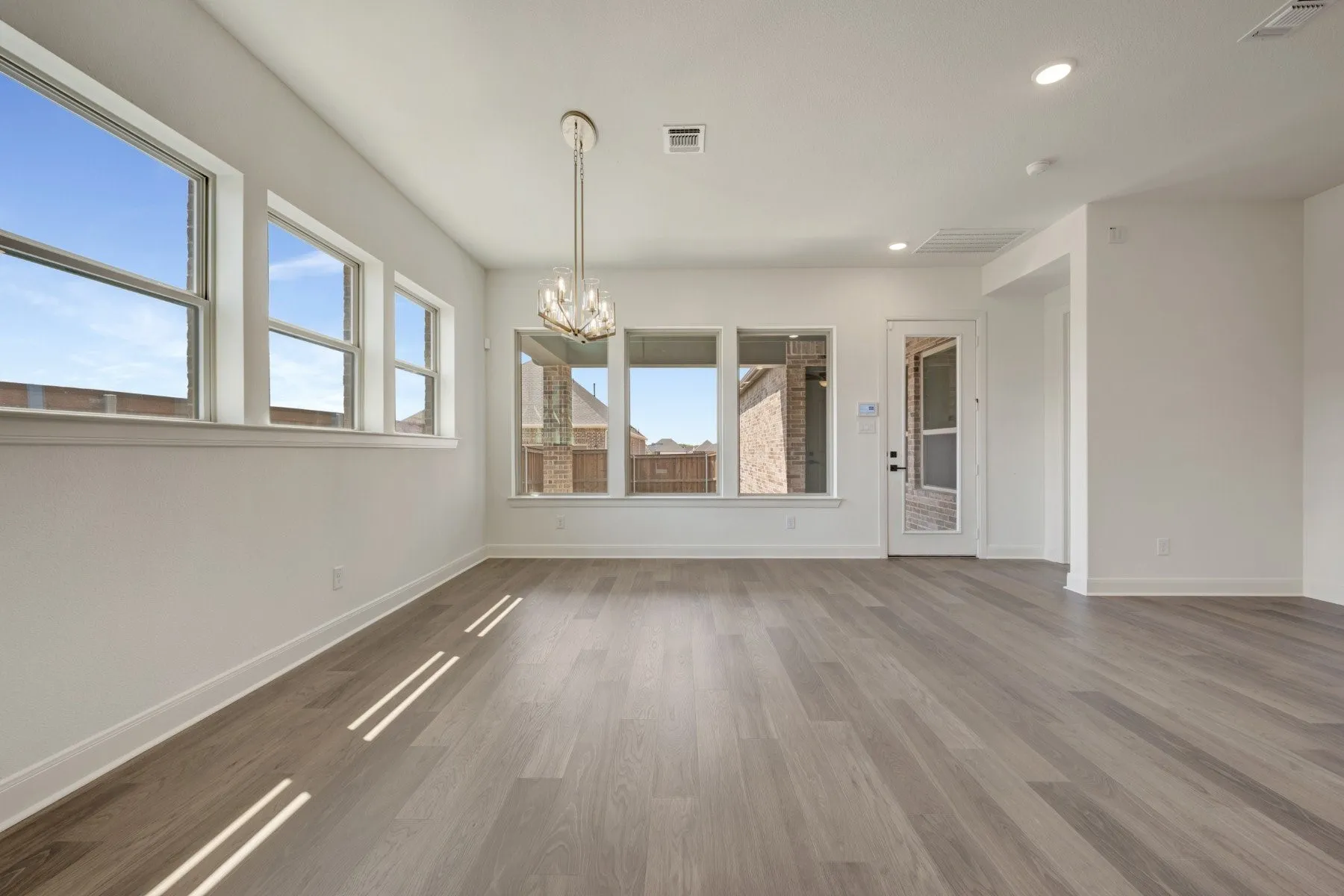 Wood-finish flooring with white baseboards, multiple windows, and a chandelier with a polished chrome finish
