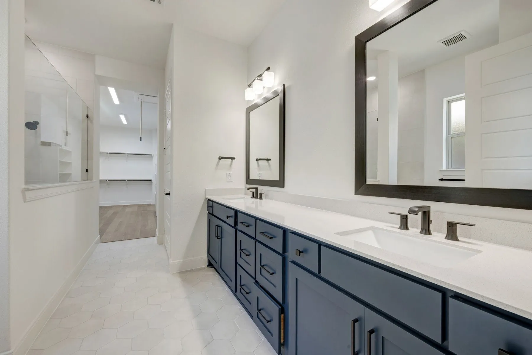 Dual vanity with dark blue cabinetry, white countertop, and dark-framed mirrors