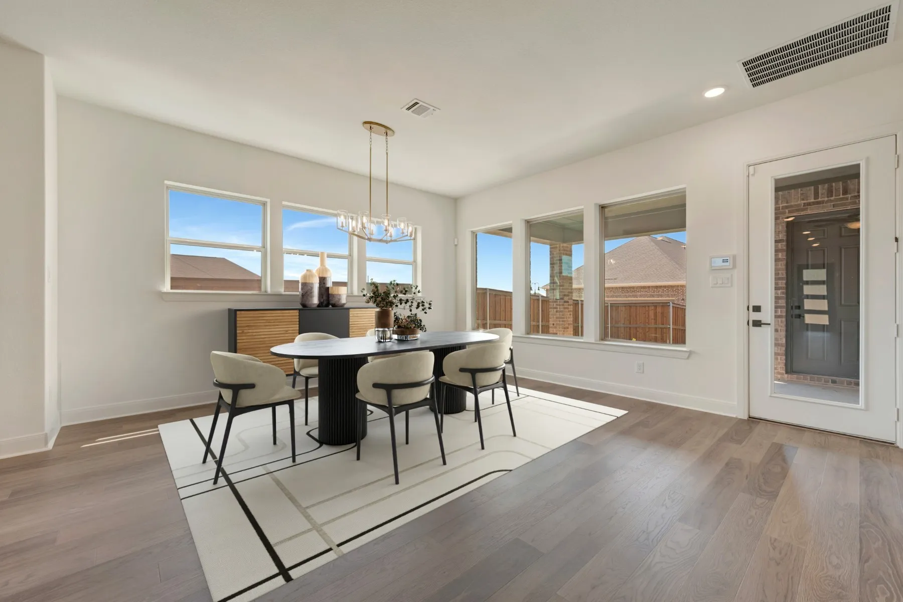 Wood-finish flooring throughout, featuring a rectangular chandelier, multiple windows, recessed lighting, and a glass-paneled door