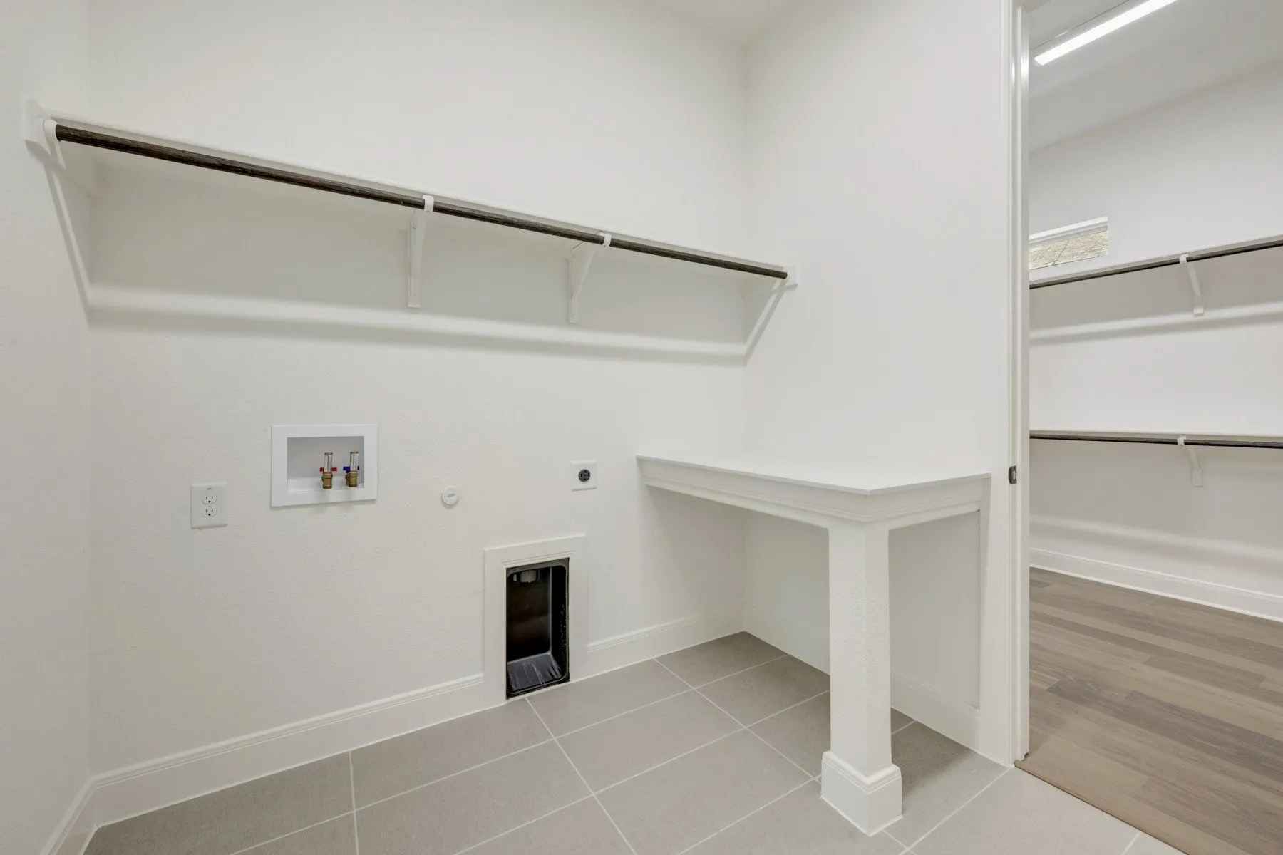 Laundry room featuring tile flooring, built-in shelving, a dedicated counter space, and an adjacent closet with wood-finish flooring