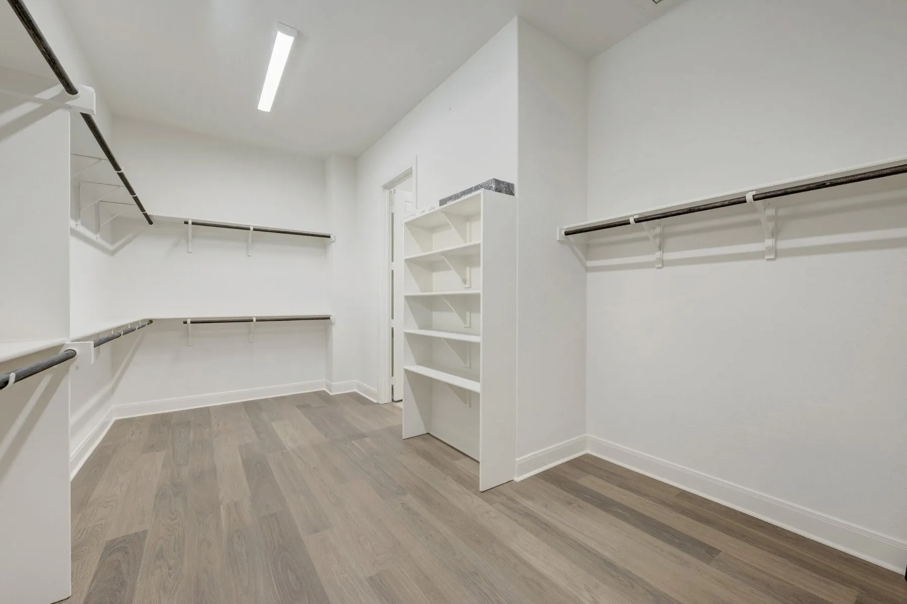 Spacious walk-in closet featuring wood-finish flooring, ample white shelving, multiple hanging rods, and recessed lighting