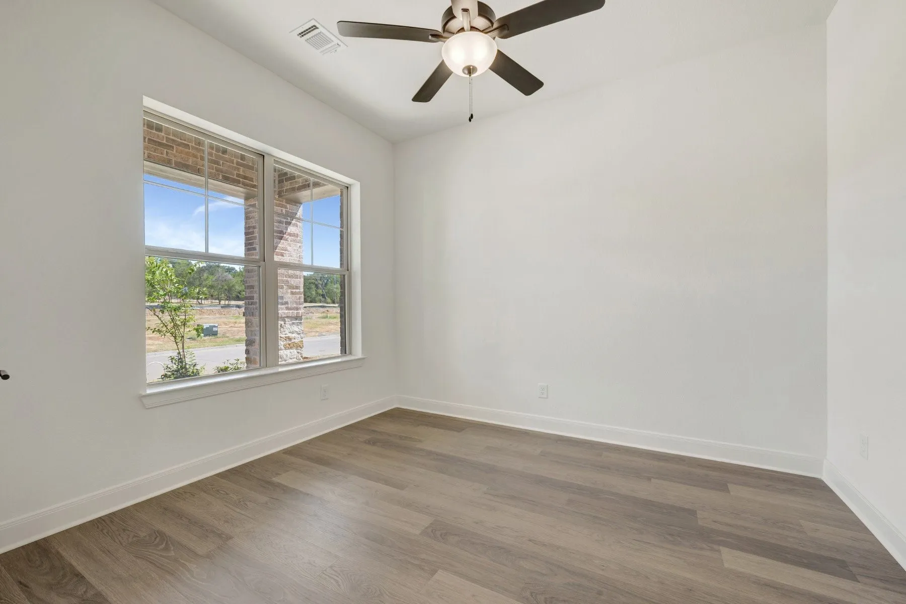 Spacious room featuring wood-finish flooring, a contemporary ceiling fan with integrated lighting, and a large window with white trim