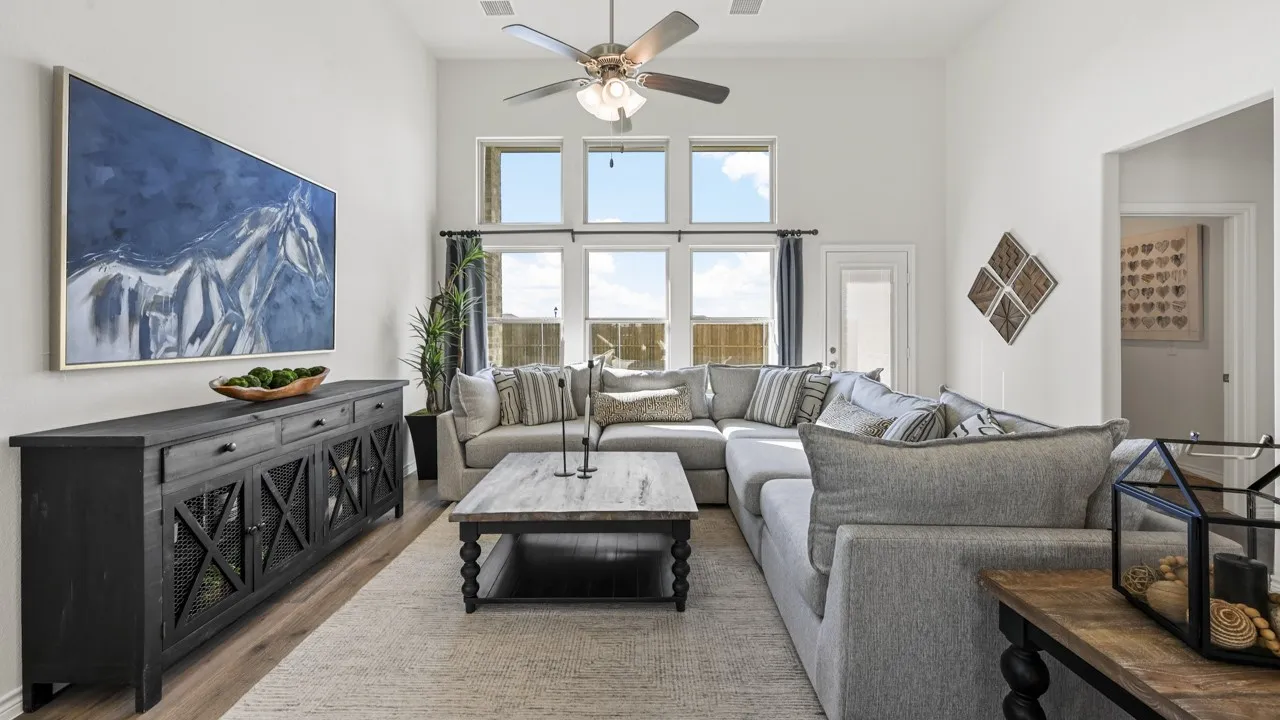Spacious living area featuring high ceilings, ample natural light from multiple windows, wood-finish flooring, and a ceiling fan