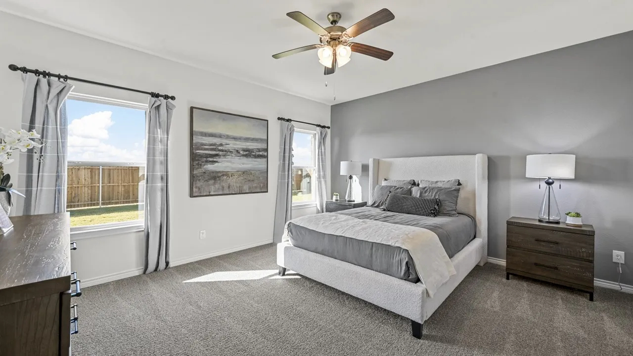 Spacious bedroom featuring neutral carpeting, a dual-pane window offering exterior views, and a ceiling fan with integrated lighting