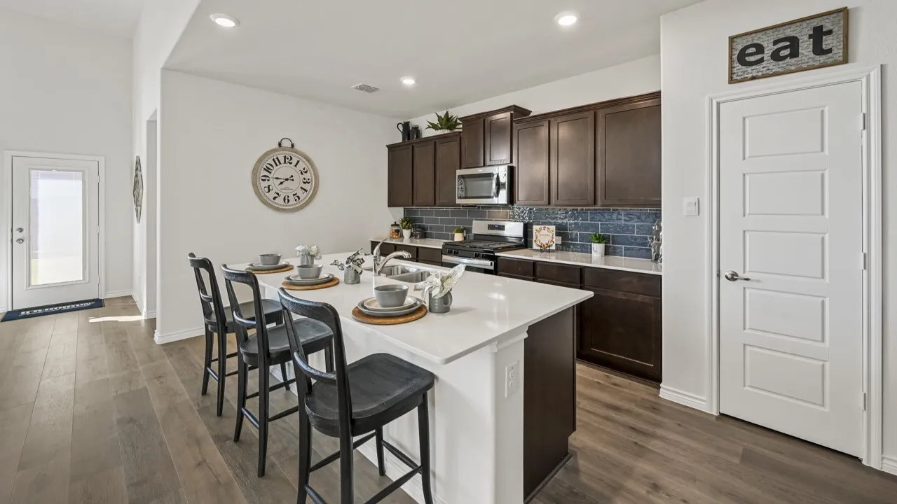 Kitchen featuring an expansive island with seating, white countertops, dark wood-finish cabinetry, stainless steel appliances, and a blue subway tile backsplash