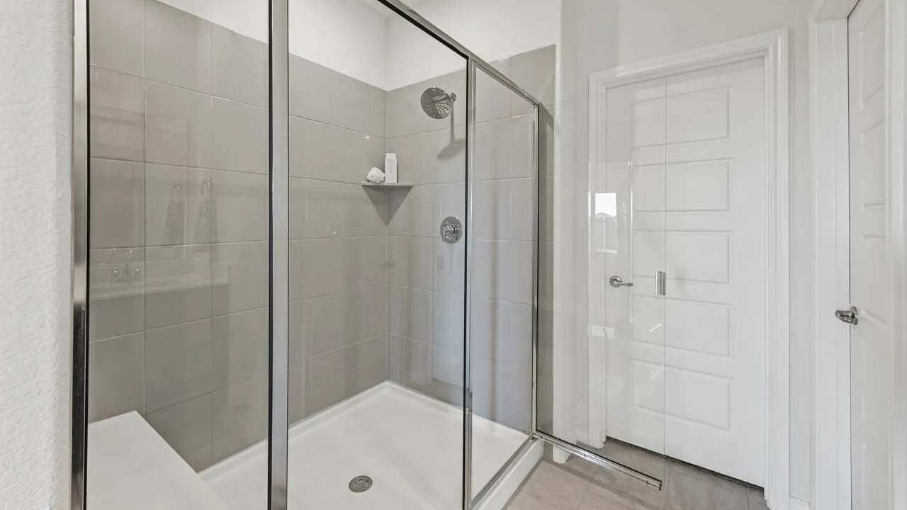 Walk-in shower with clear glass enclosure, gray subway tile surround, integrated shower bench, and corner shelf