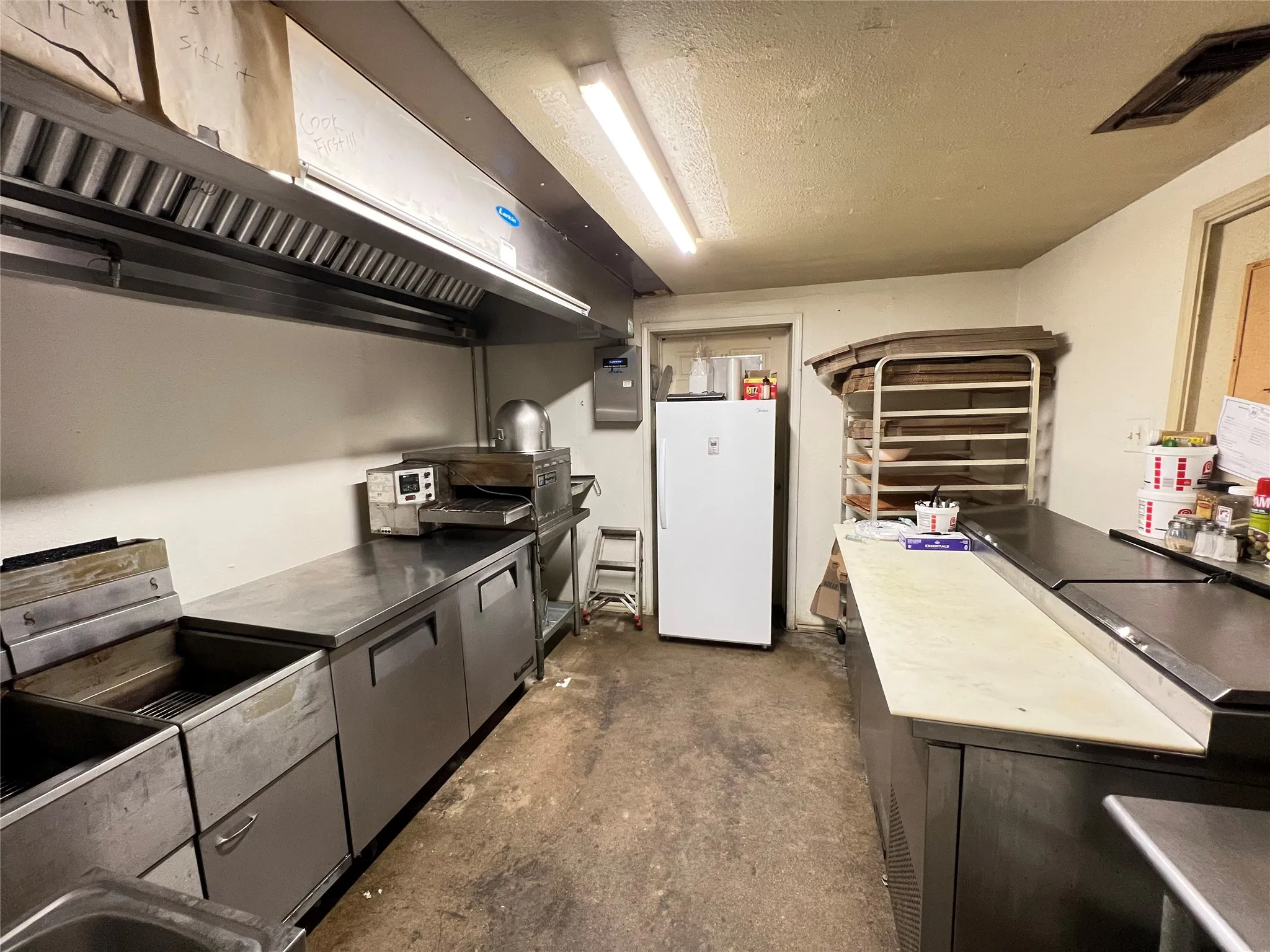 Commercial kitchen featuring stainless steel countertops, built-in sinks, and an overhead ventilation system