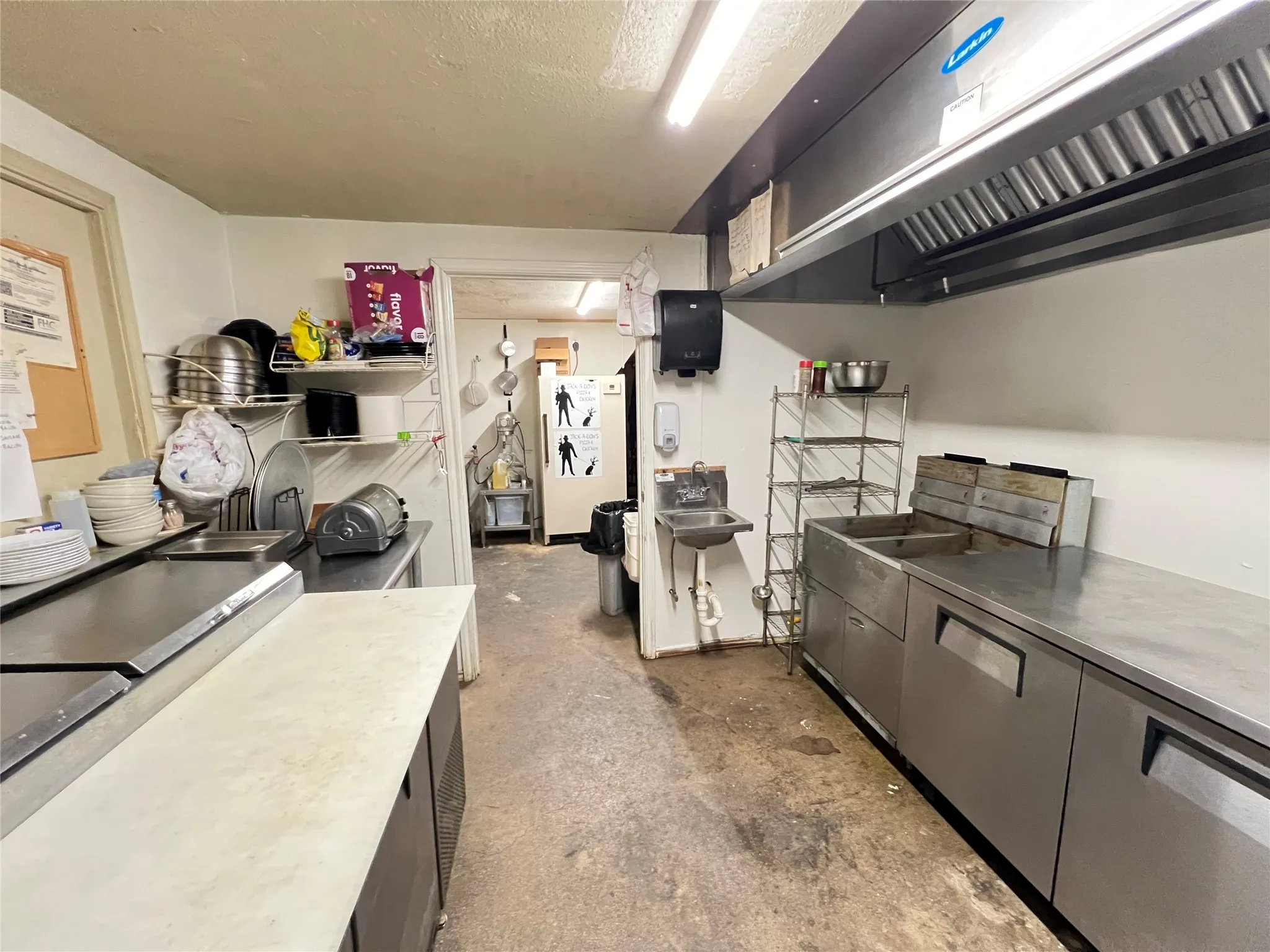 Commercial kitchen featuring stainless steel work surfaces, a large ventilation hood, a built-in sink, and a wall-mounted hand wash station
