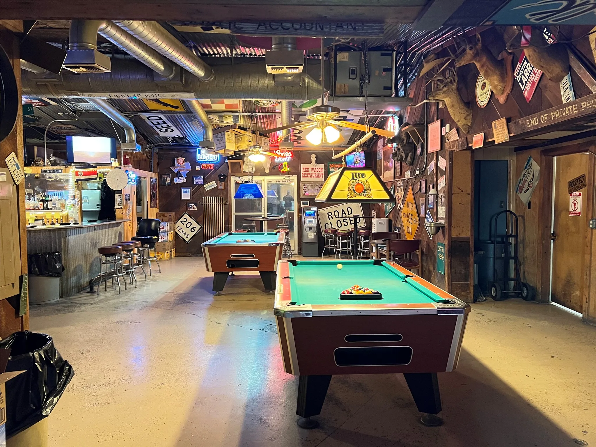 Recreational room featuring two billiard tables, a bar area with seating, and exposed ceiling ductwork
