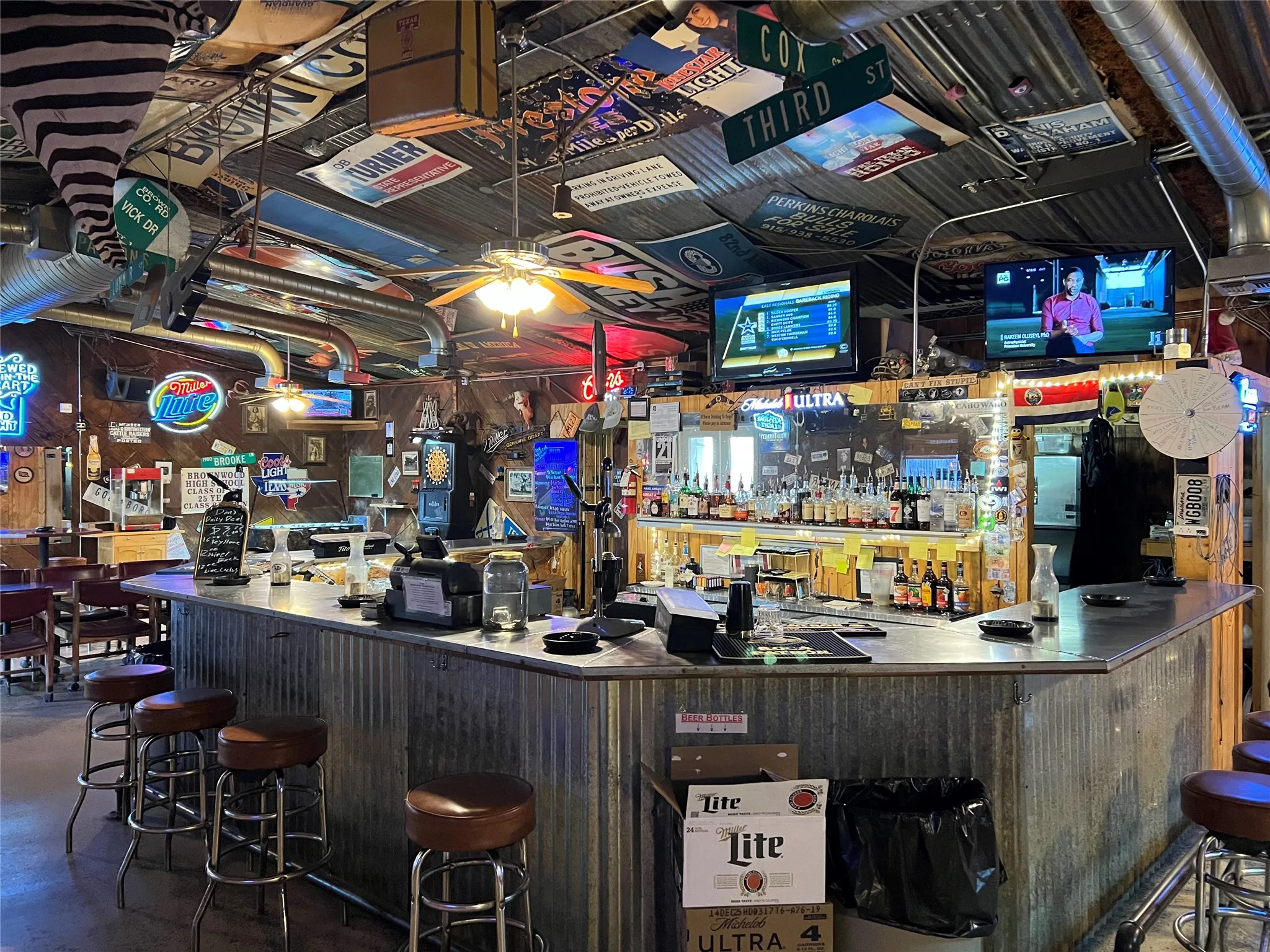 Corrugated metal bar with a light-toned counter surface, accompanied by multiple bar stools featuring dark brown upholstered seats