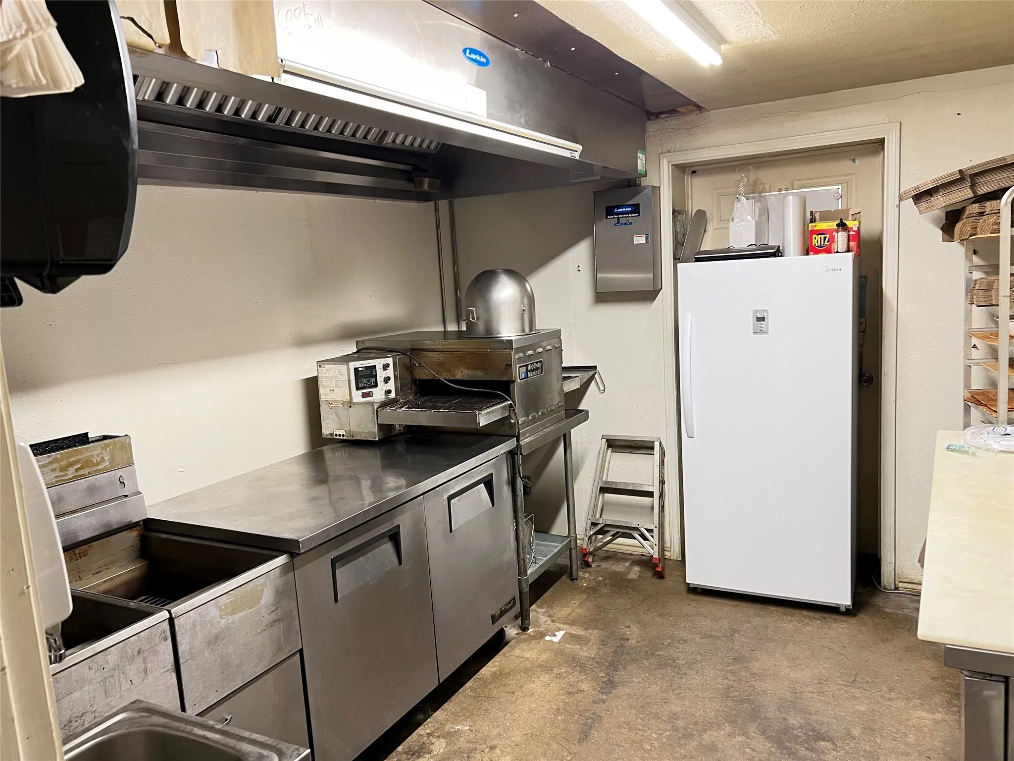 Commercial kitchen space featuring a stainless steel hood vent, stainless steel prep counters, and a built-in stainless steel sink