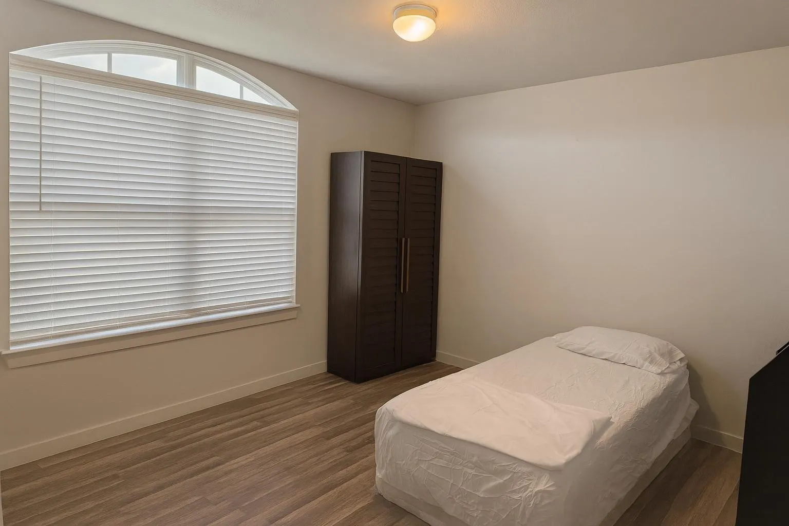 Room with an arched window featuring horizontal blinds, wood-finish flooring, and a flush-mount ceiling light fixture