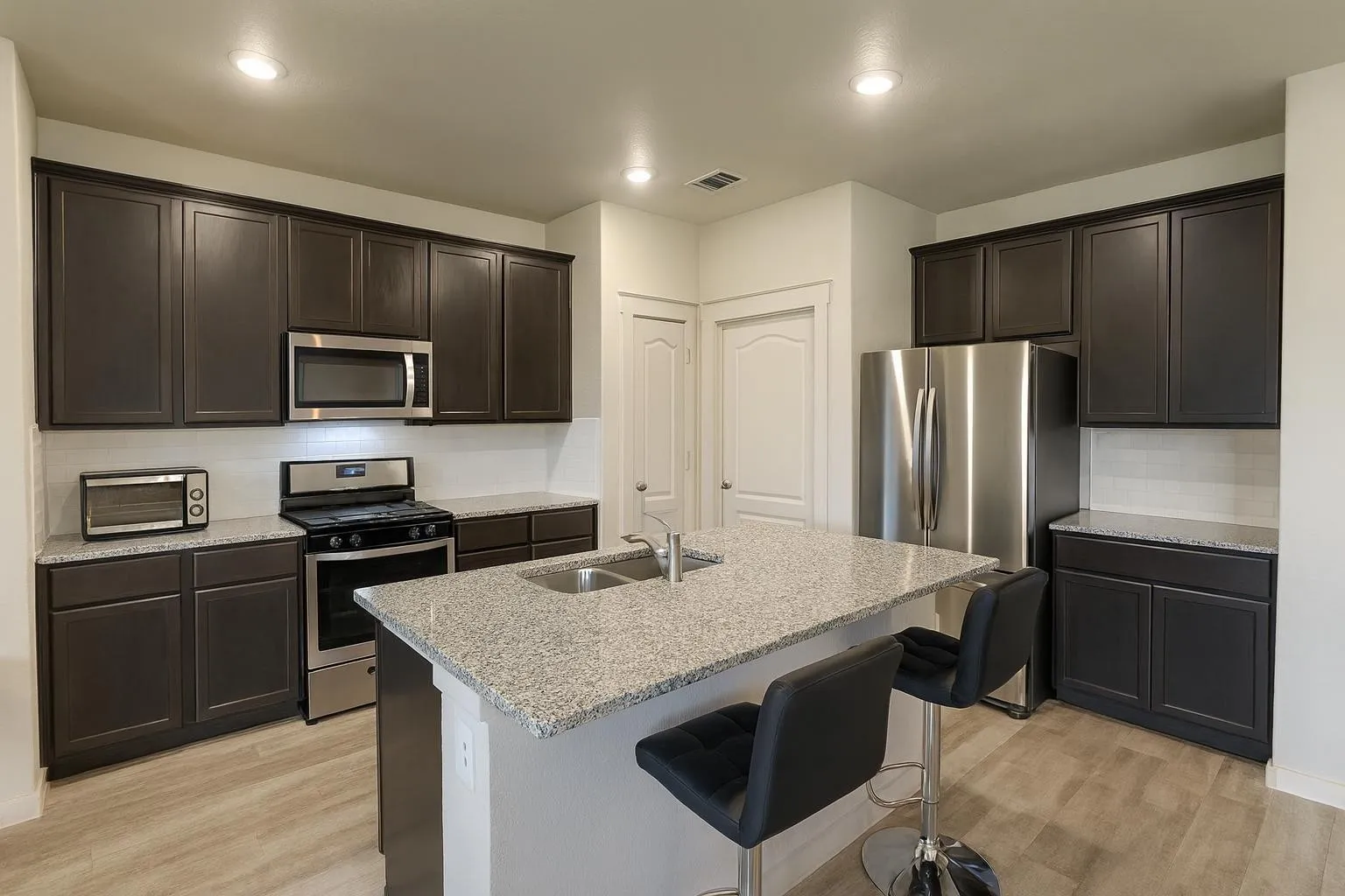 Contemporary kitchen featuring dark wood-finish cabinetry, stainless steel appliances, granite countertops, and wood-look flooring