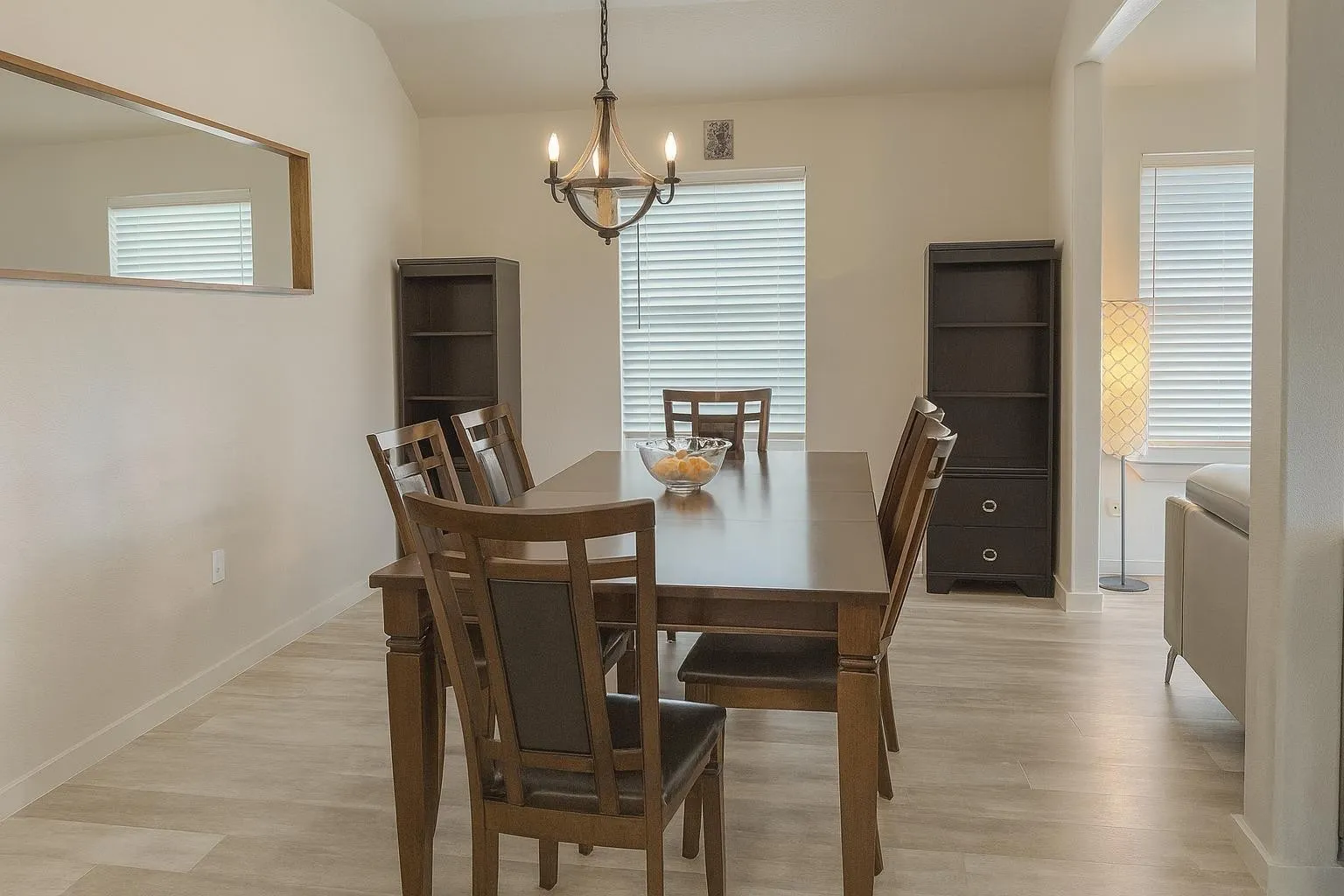 Vaulted ceiling dining area with wood-finish flooring, a contemporary chandelier, multiple windows with blinds, and a built-in wall niche