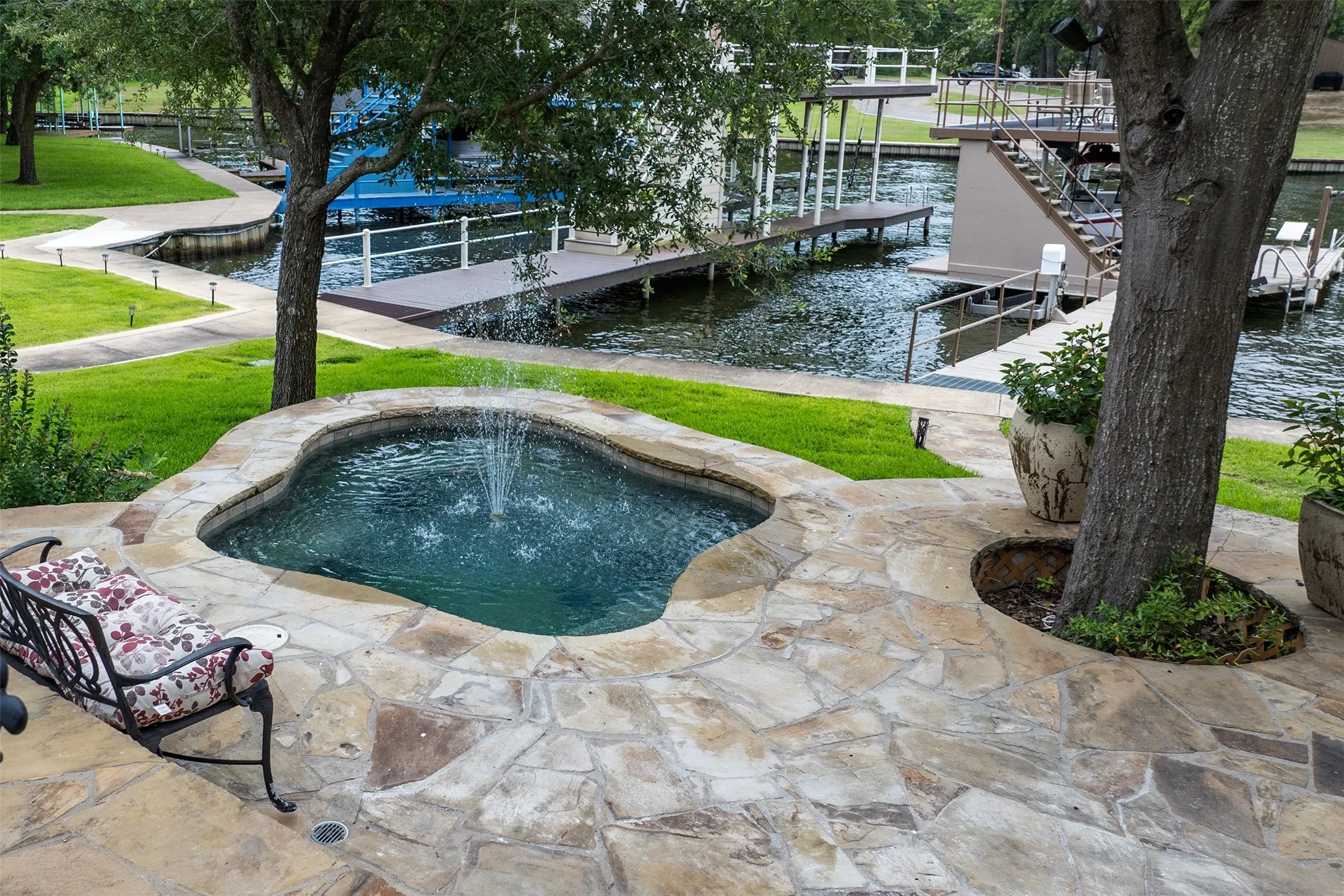 Irregular flagstone patio featuring a built-in spa with a water feature, surrounded by manicured lawn and mature trees