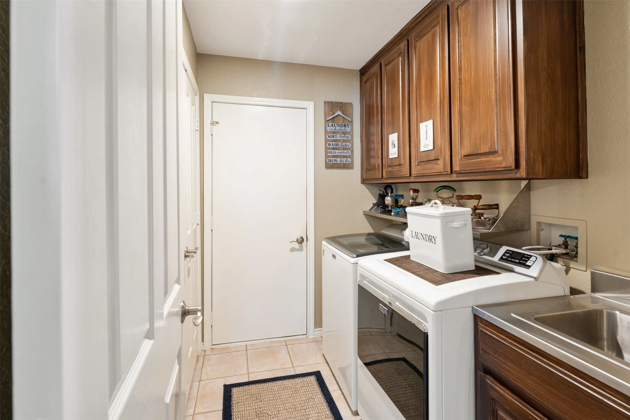 Utility space featuring wood cabinetry, a stainless steel utility sink, and tile flooring