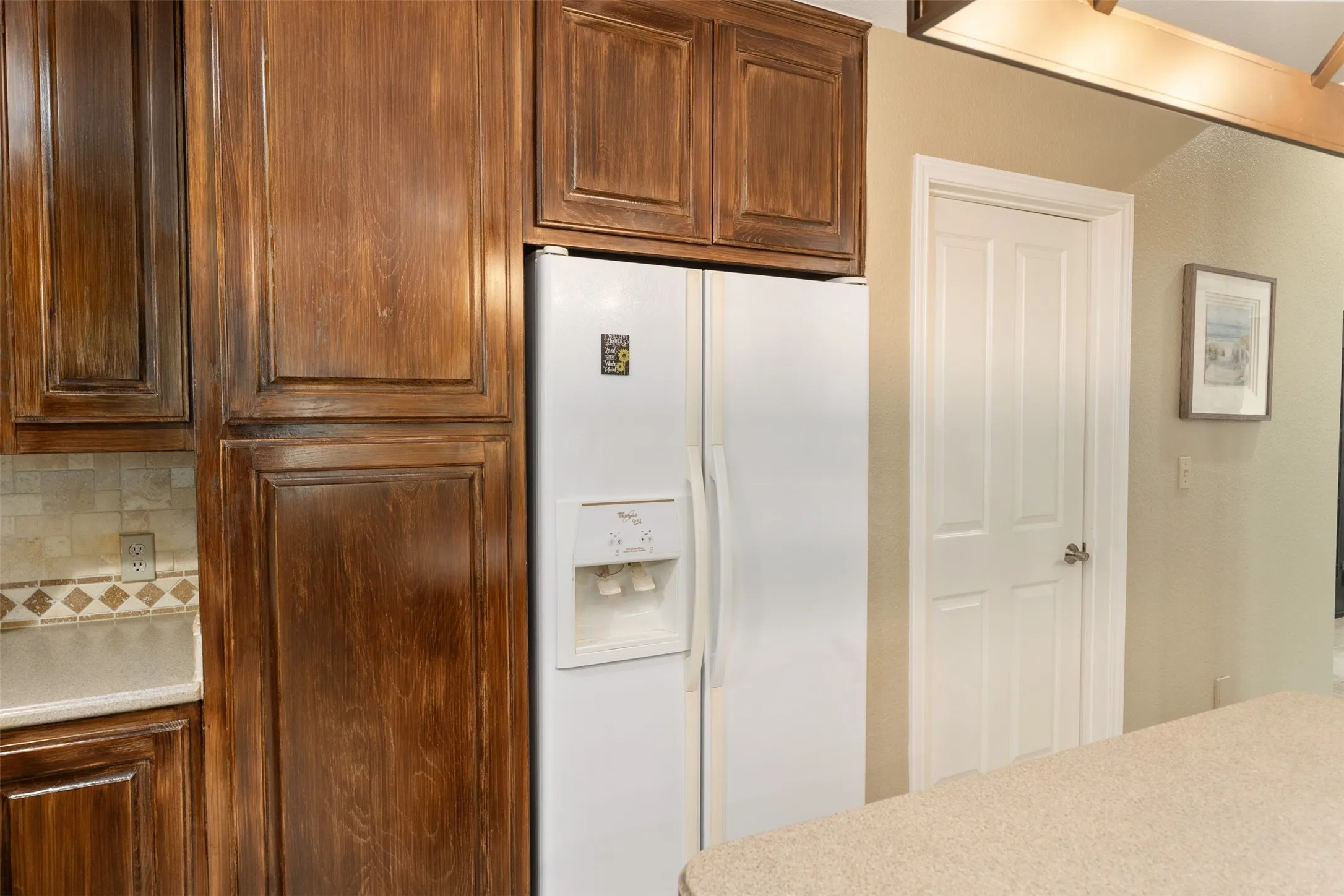 Kitchen area featuring rich wood-finish cabinetry, tile backsplash with decorative accents, and light-toned countertops