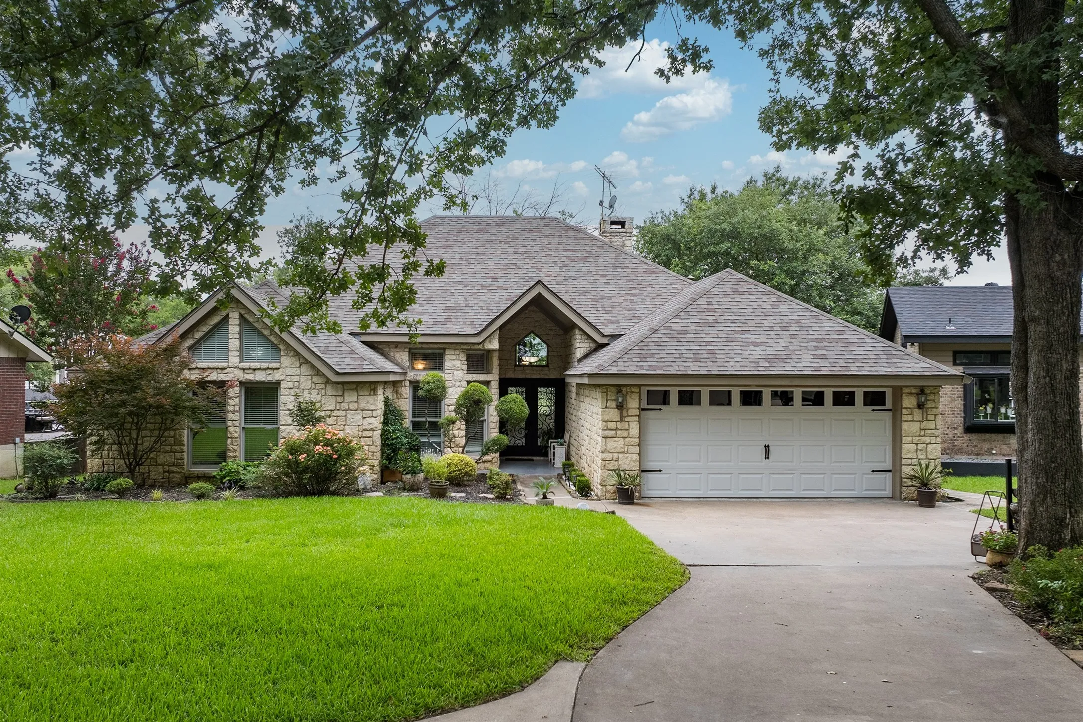 Stone façade residence featuring a gabled roofline, an attached two-car garage, and a concrete driveway