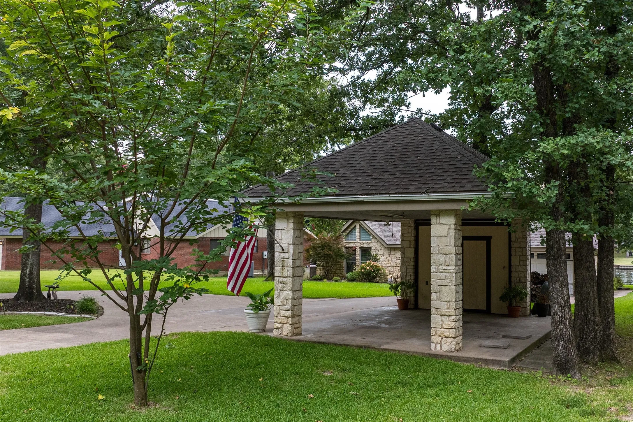Stone-clad portico featuring a dark shingle roof and concrete flooring
