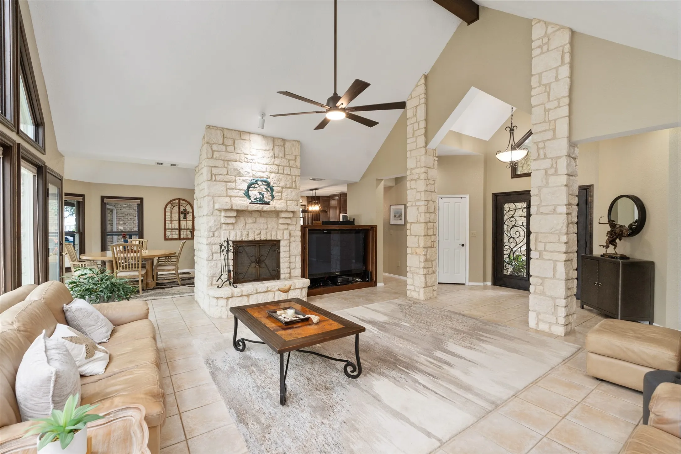Vaulted ceiling living space featuring a stone fireplace, exposed beams, and tile flooring
