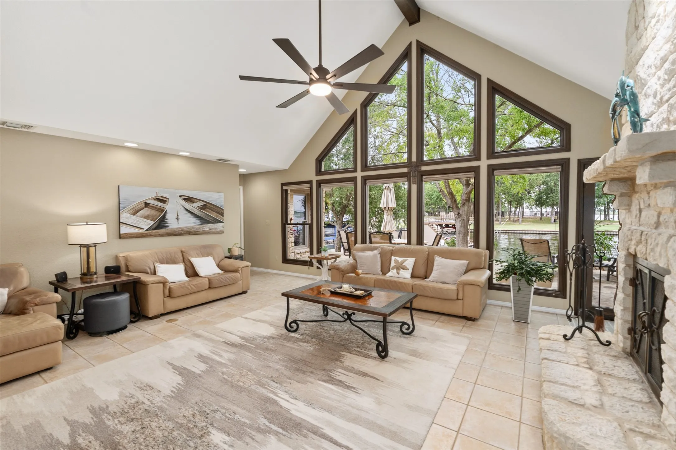 Spacious living area featuring a vaulted ceiling with exposed beams, an expansive wall of windows, and light-toned tile flooring