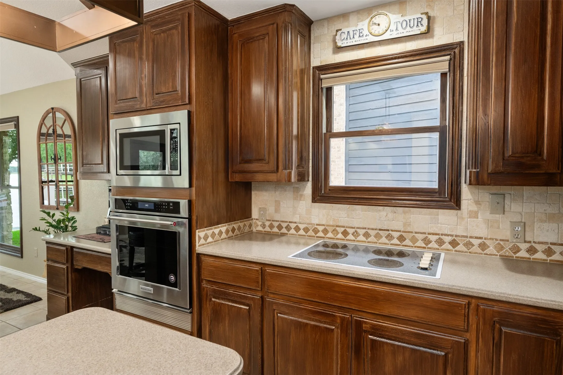 Kitchen featuring wood cabinetry, light-toned countertops, tile backsplash with decorative accents, and built-in stainless steel appliances